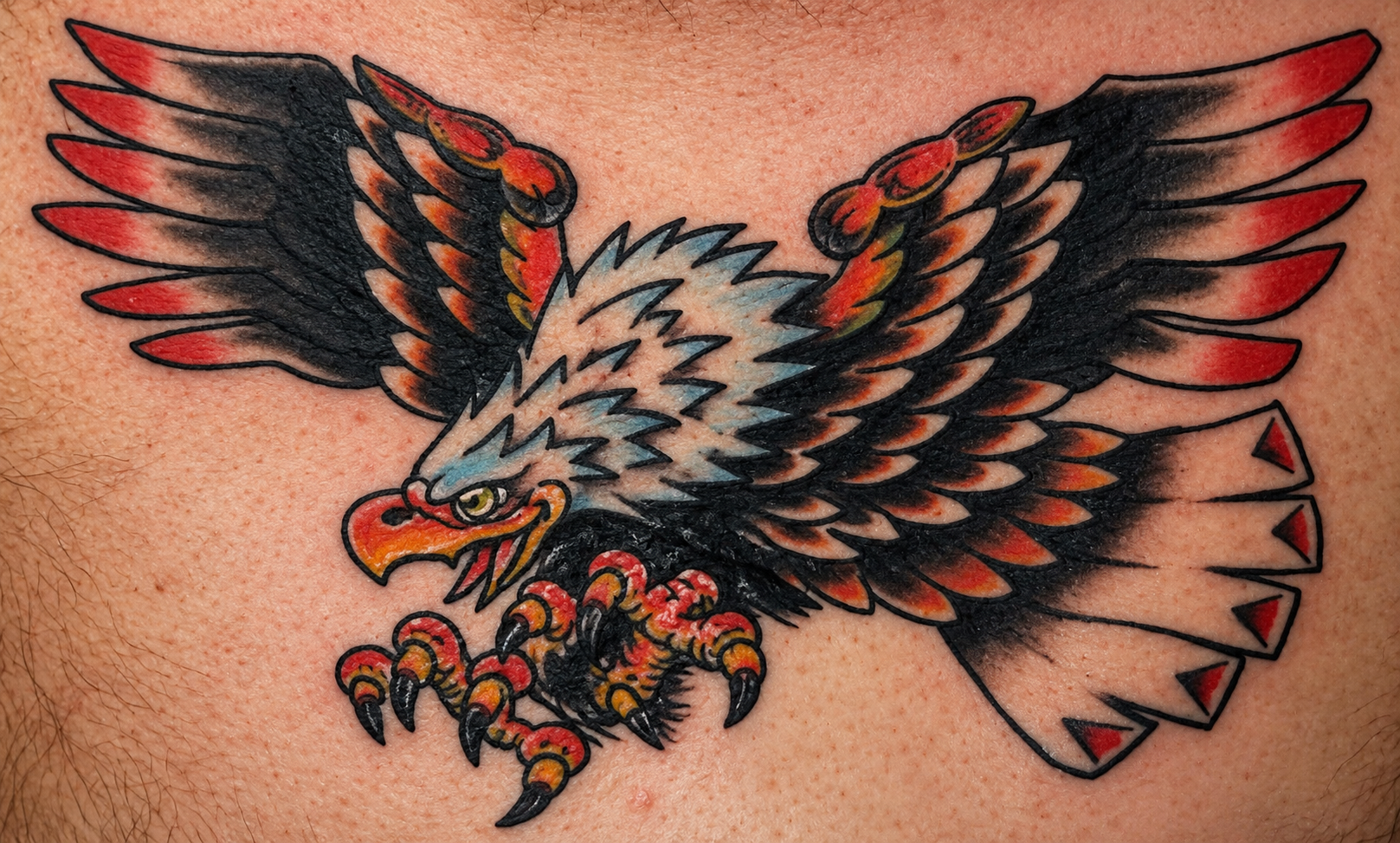 Colorful tattoo of an aggressive bald eagle in flight with wings spread wide and talons extended, featuring black, white, red, orange, and yellow shading.