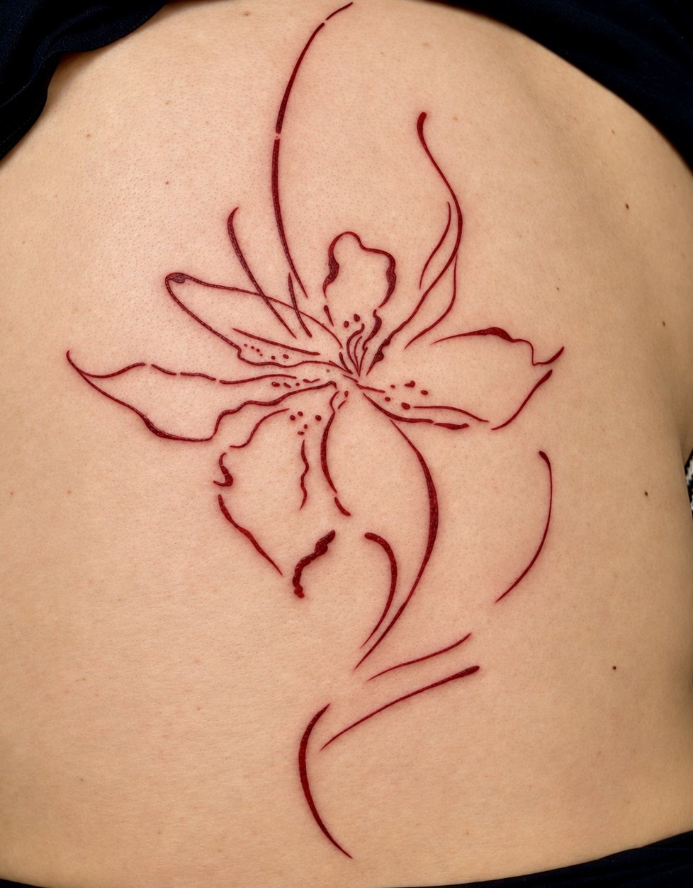 Tattoo of a stylized flower with elongated petals and swirling lines on a person's back.