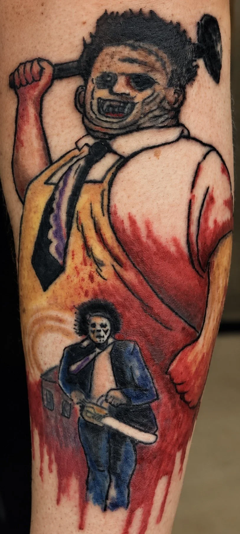 Tattoo of a character with dark short hair, sunglasses, and a big smile, holding an axe. Below is a smaller character in a suit and mask, holding a weapon, with a red and yellow background.