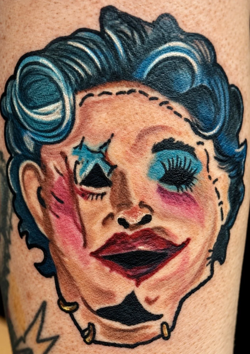 Color tattoo of a stylized woman's face with exaggerated makeup and features, including blue eyeshadow, bright pink blush, bold red lipstick, and black eyeliner, with decorative black and gold earrings.