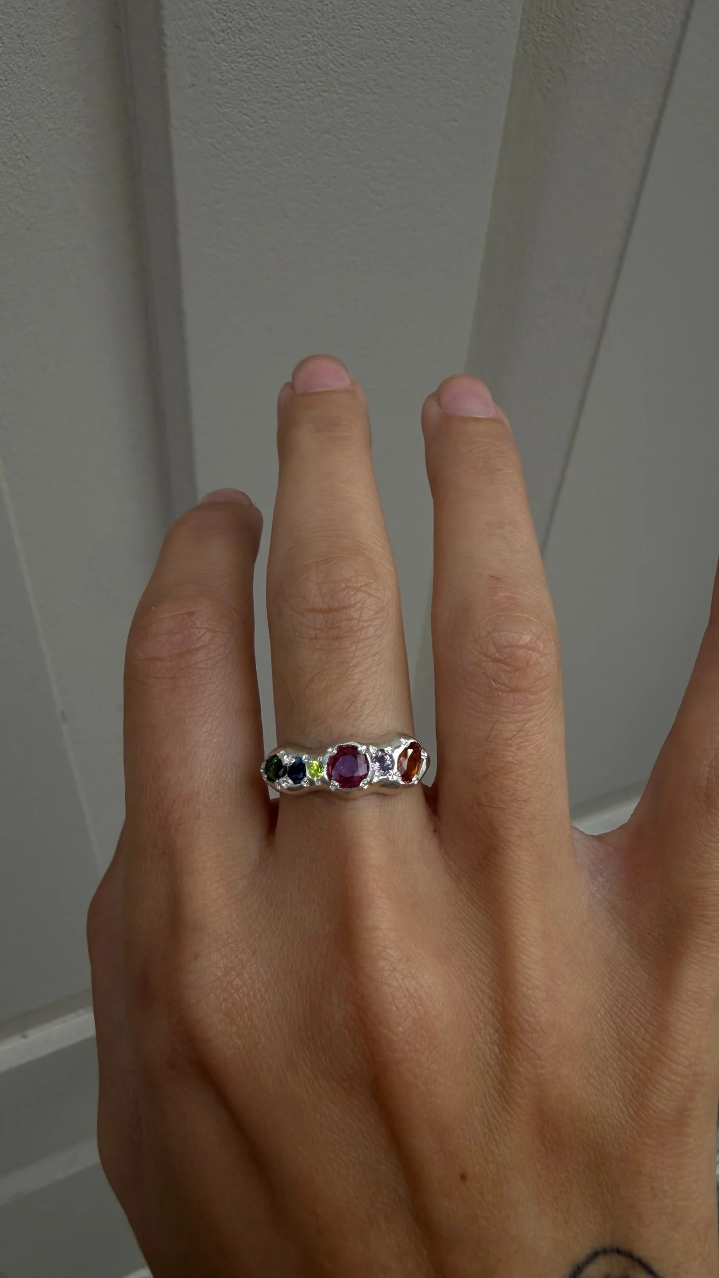 A molten silver ring with multicoloured gemstones photographed on a hand