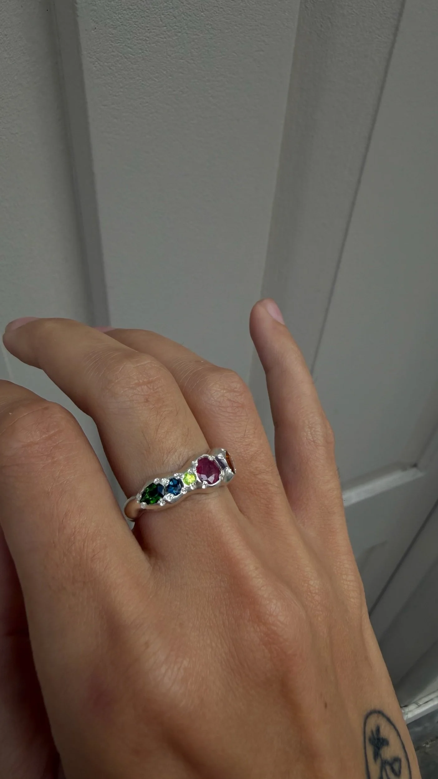A molten silver ring with multicoloured gemstones photographed on a hand