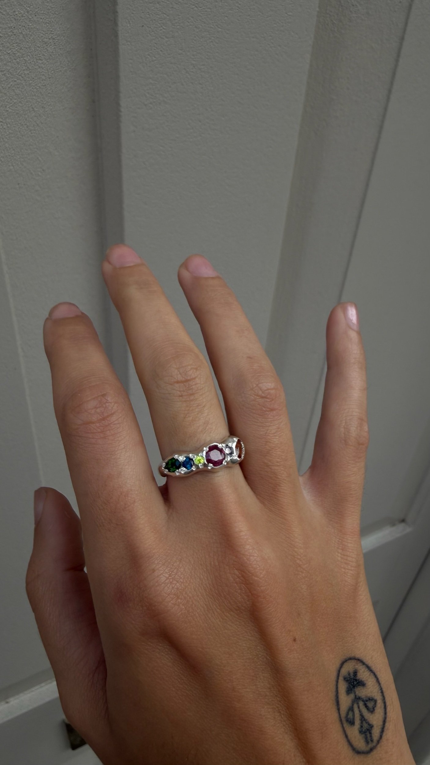A molten silver ring with multicoloured gemstones photographed on a hand