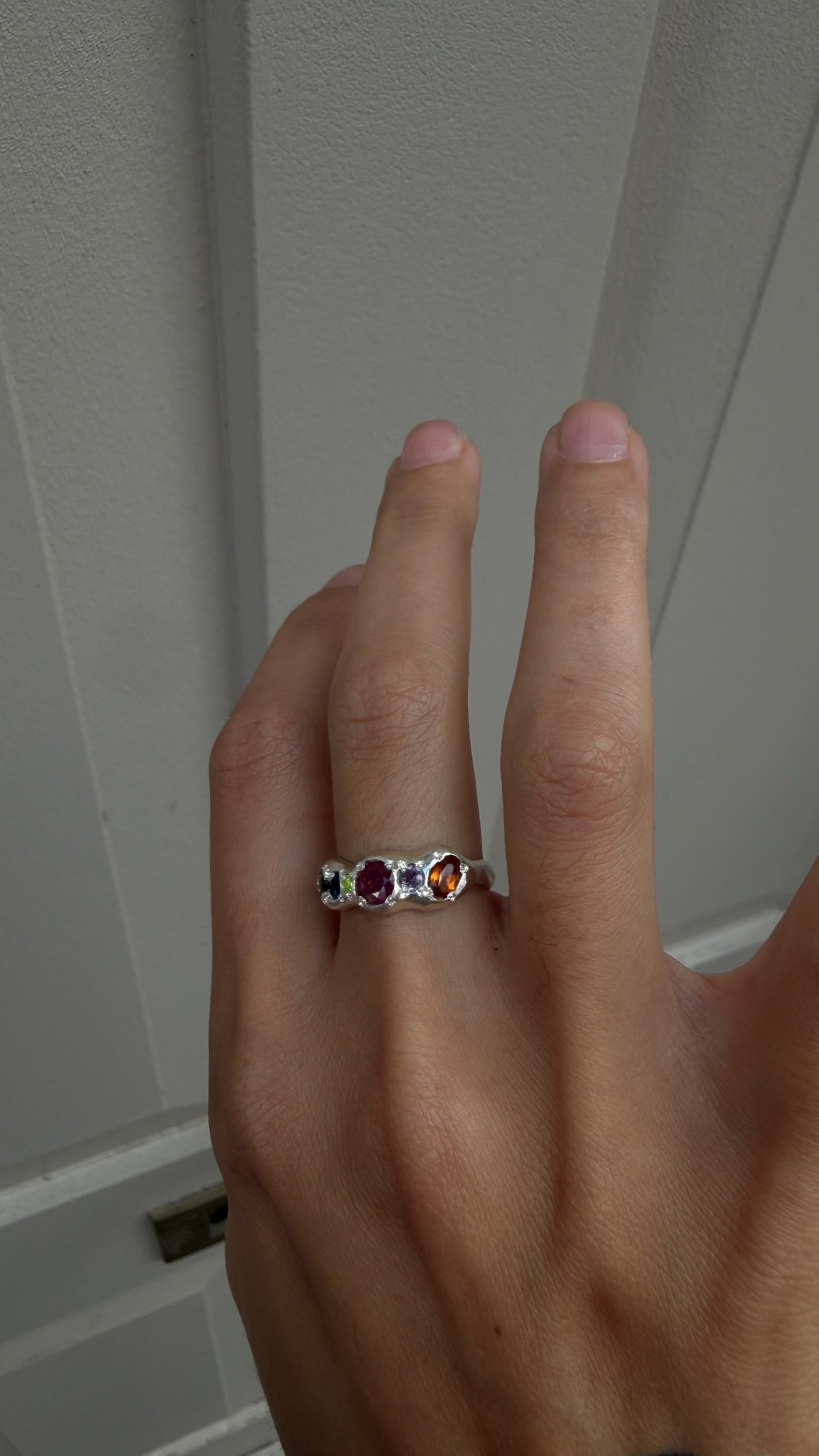 A molten silver ring with multicoloured gemstones photographed on a hand