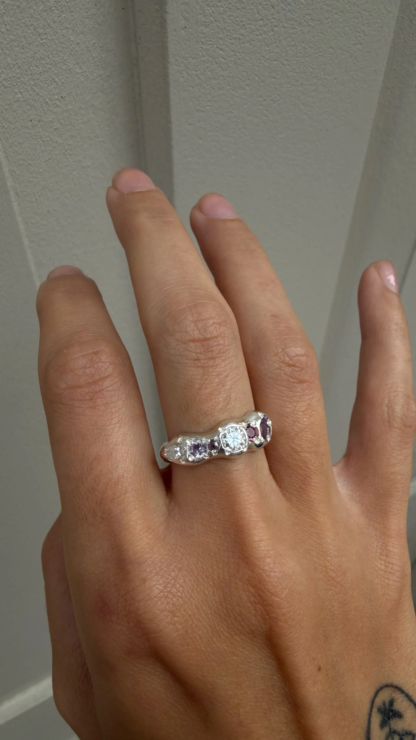 A molten silver ring with multicoloured gemstones photographed on a hand