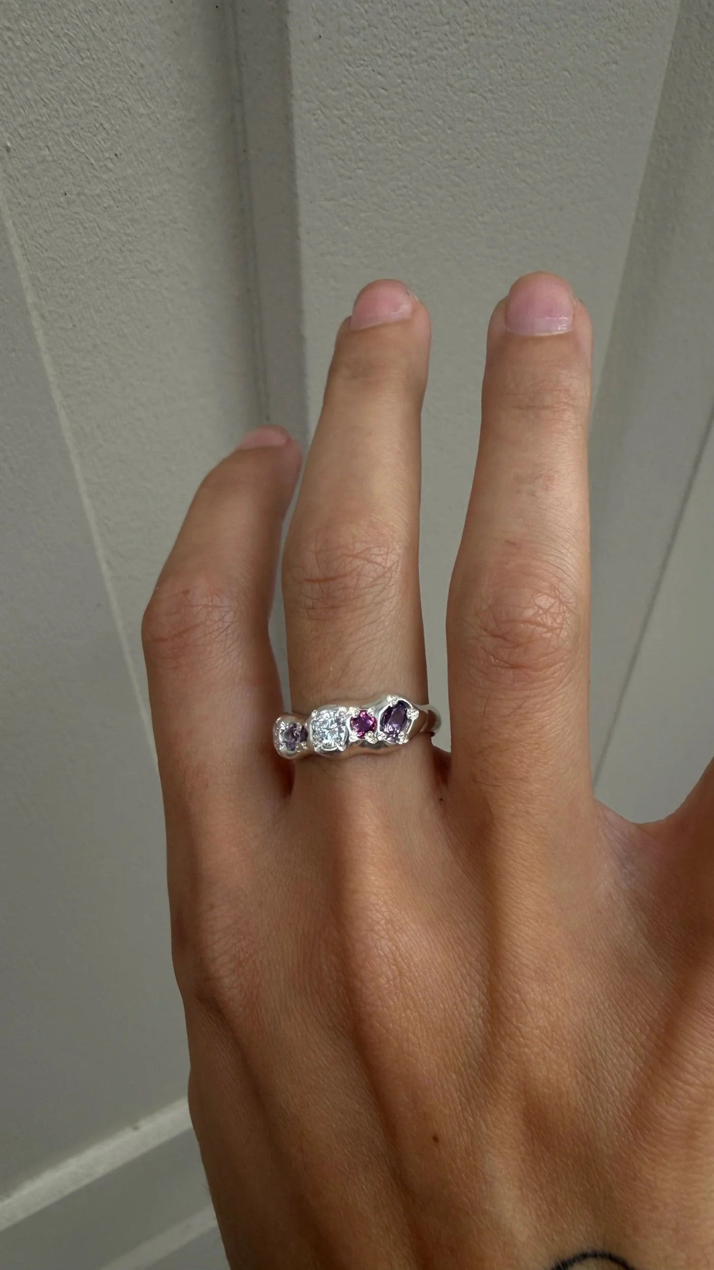 A molten silver ring with multicoloured gemstones photographed on a hand