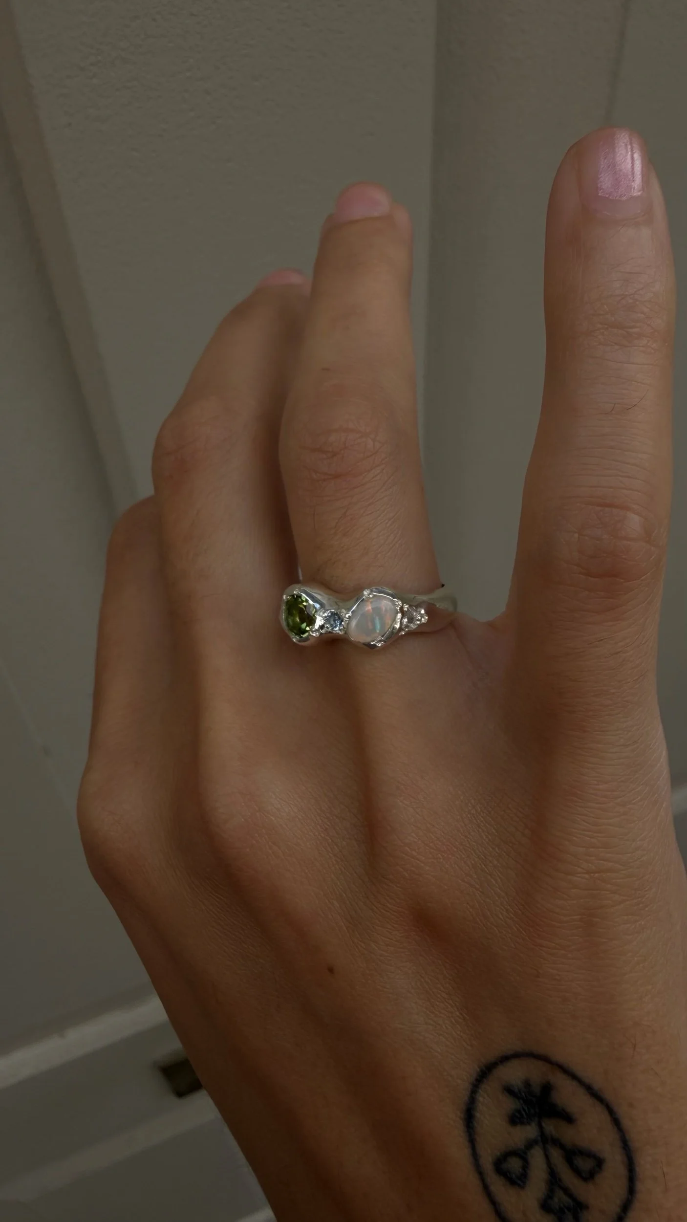 A silver ring with a opal and peridot stone as the focus on a hand