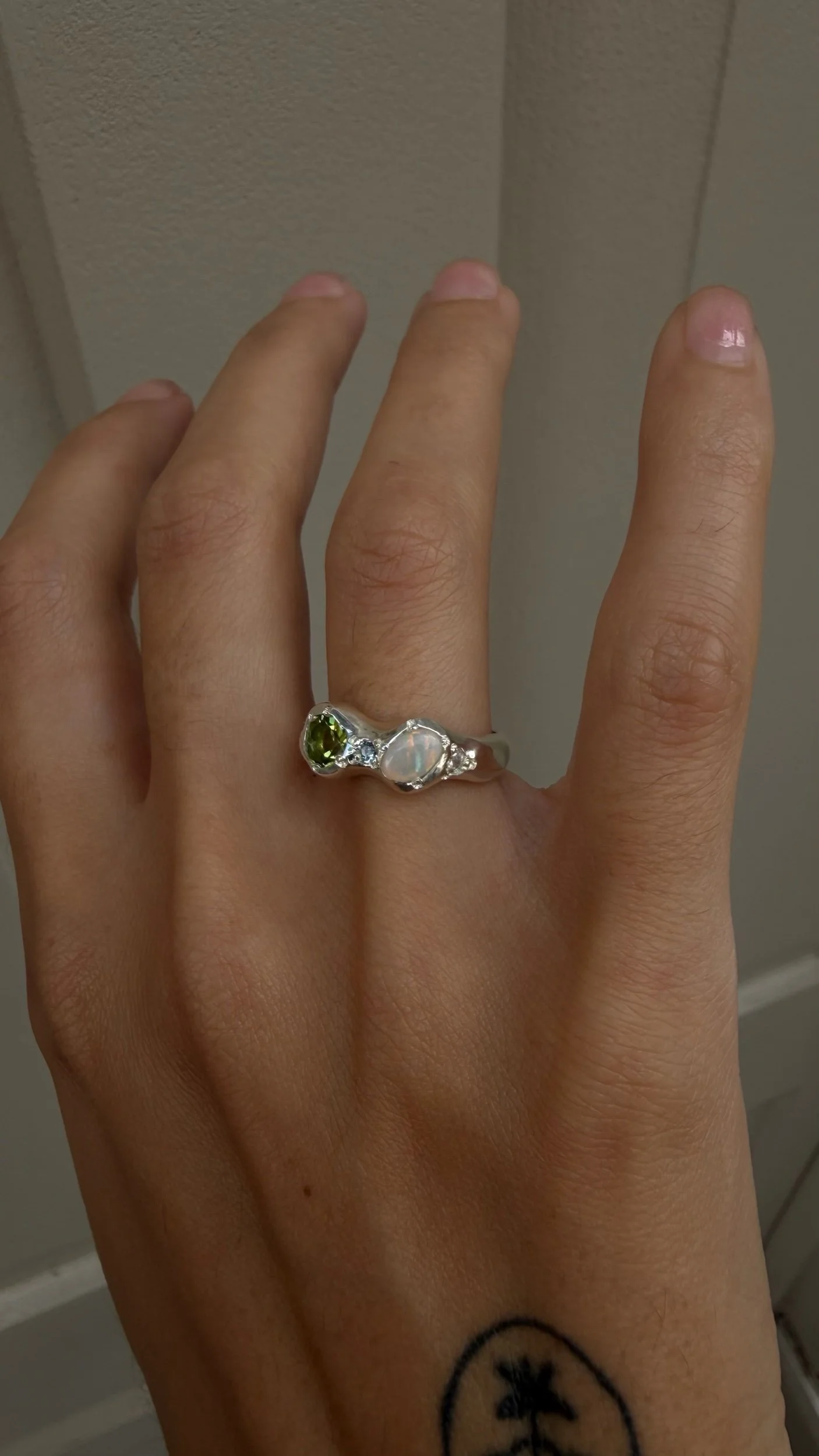 A silver ring with a opal and peridot stone as the focus on a hand