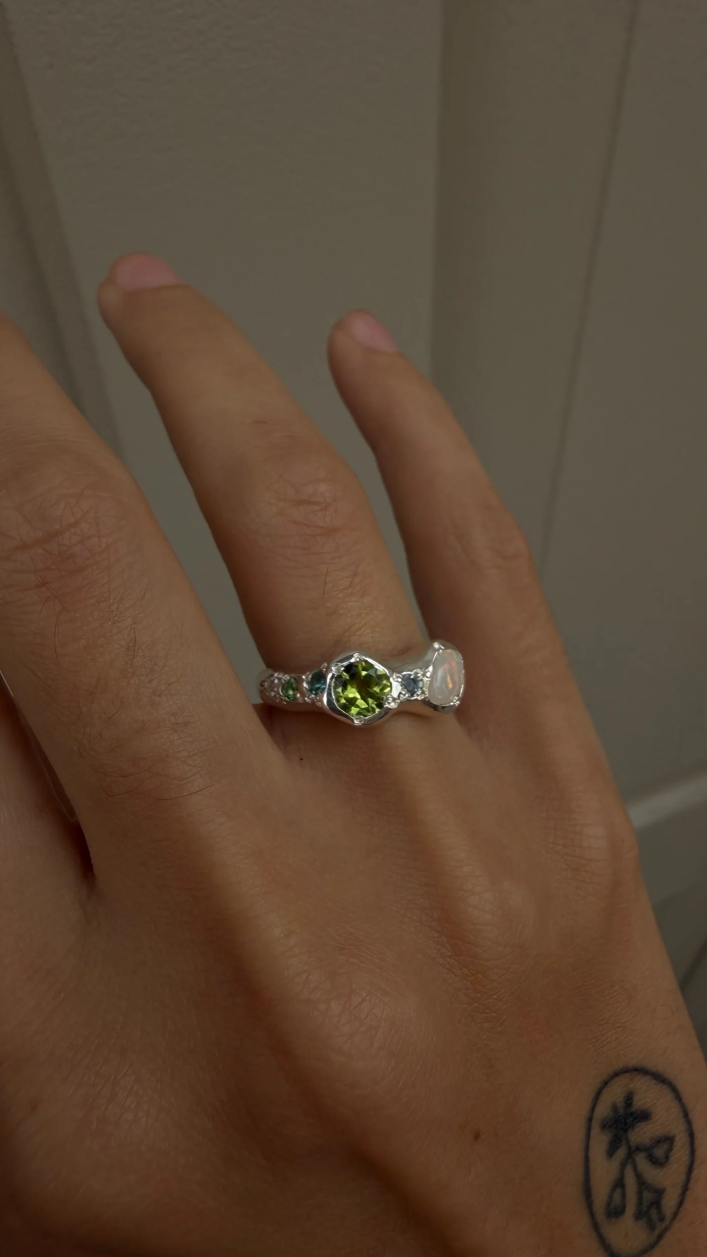 A silver ring with a opal and peridot stone as the focus on a hand