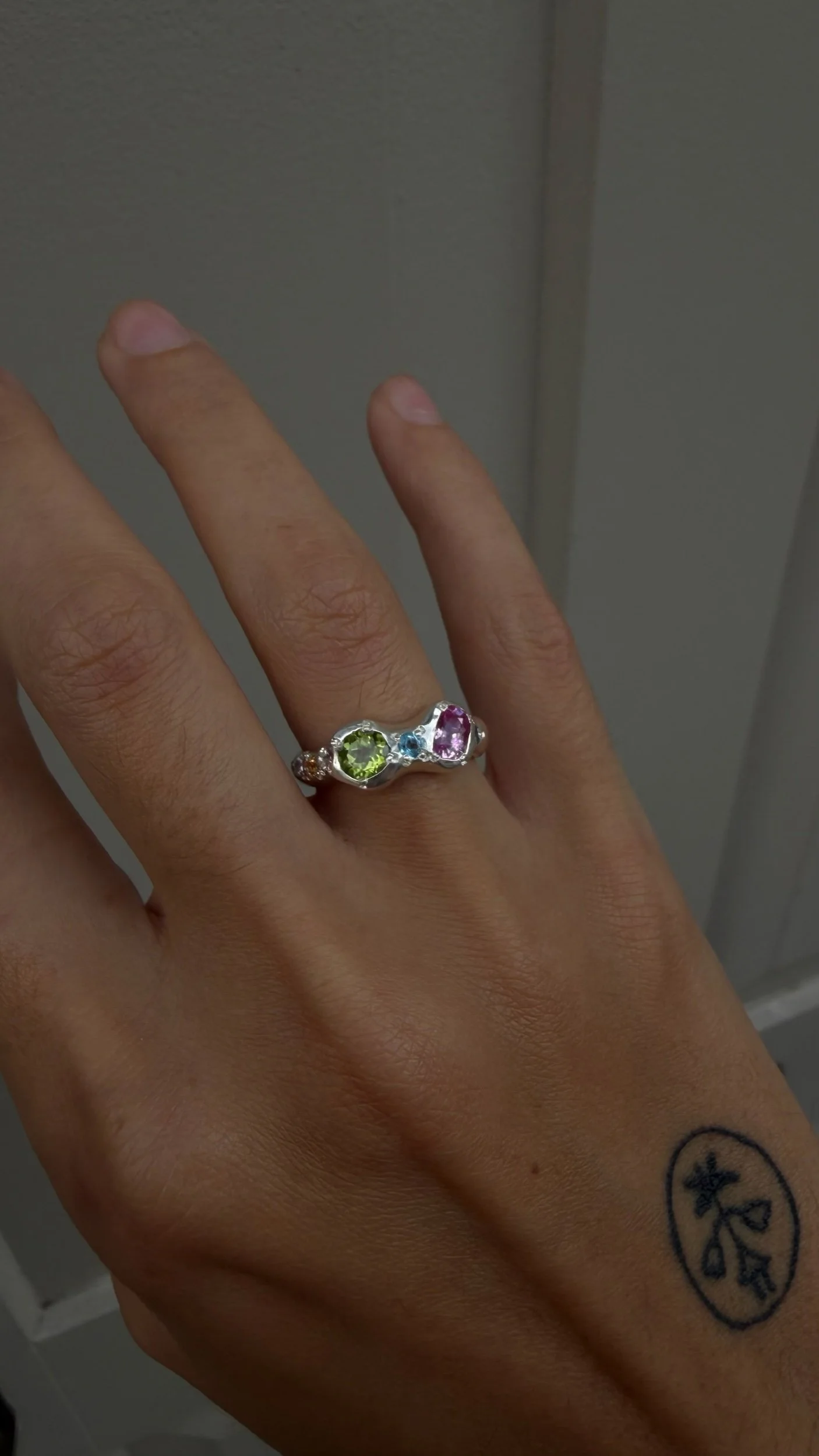A silver ring with a central green and pink stone as the focus on a hand