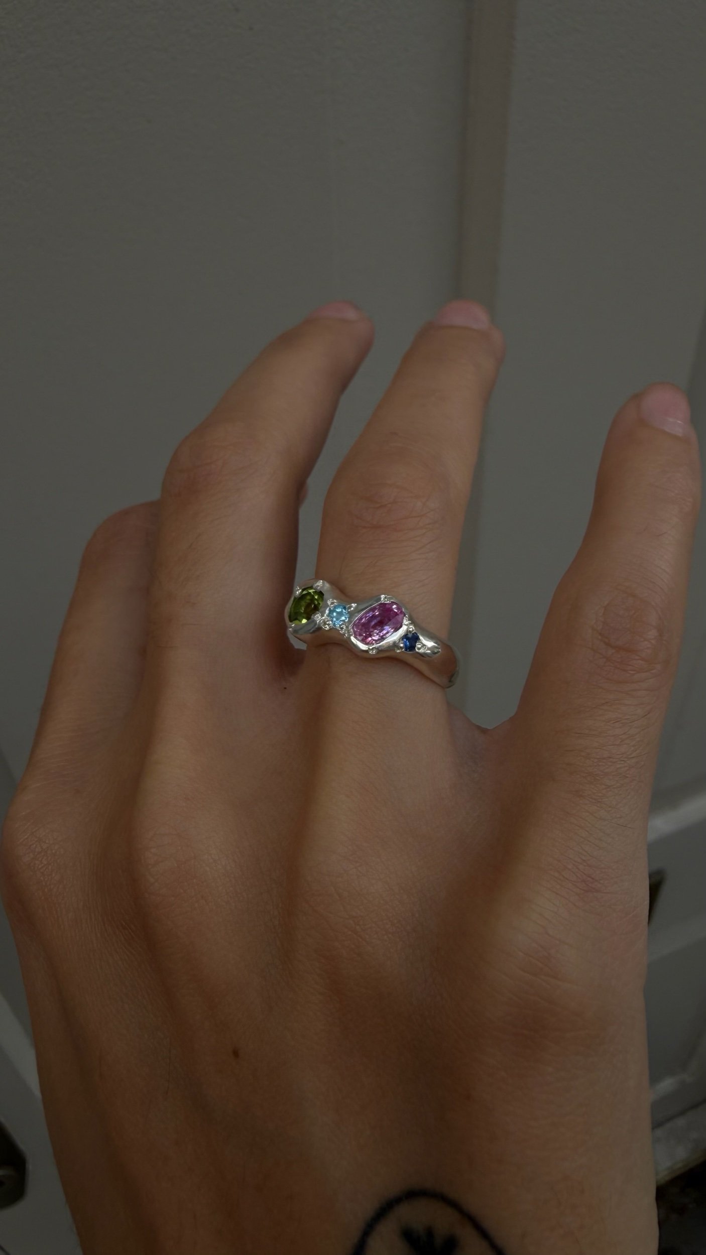 A silver ring with a central green and pink stone as the focus on a hand