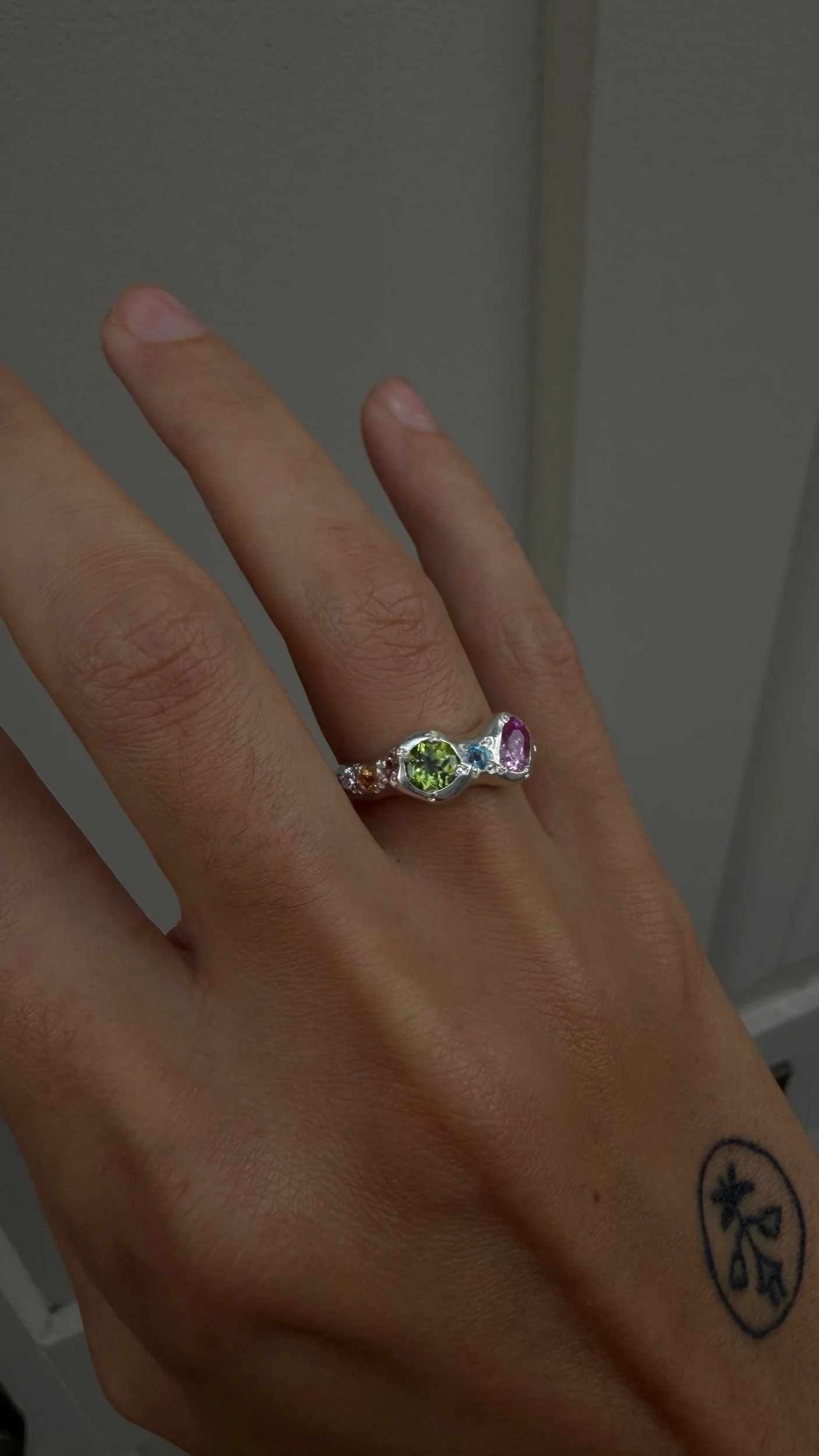 A silver ring with a central green and pink stone as the focus on a hand