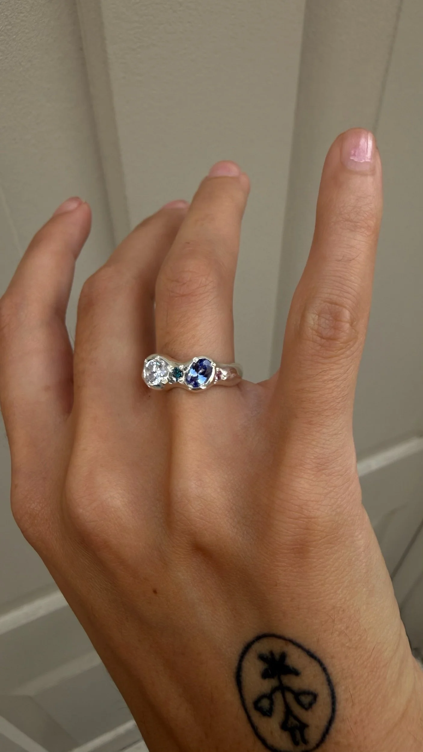 A silver ring with a white and purple stone as the focus on a hand