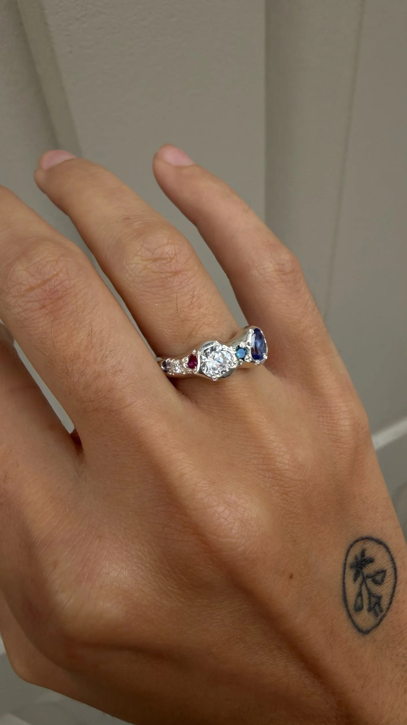 A silver ring with a white and purple stone as the focus on a hand