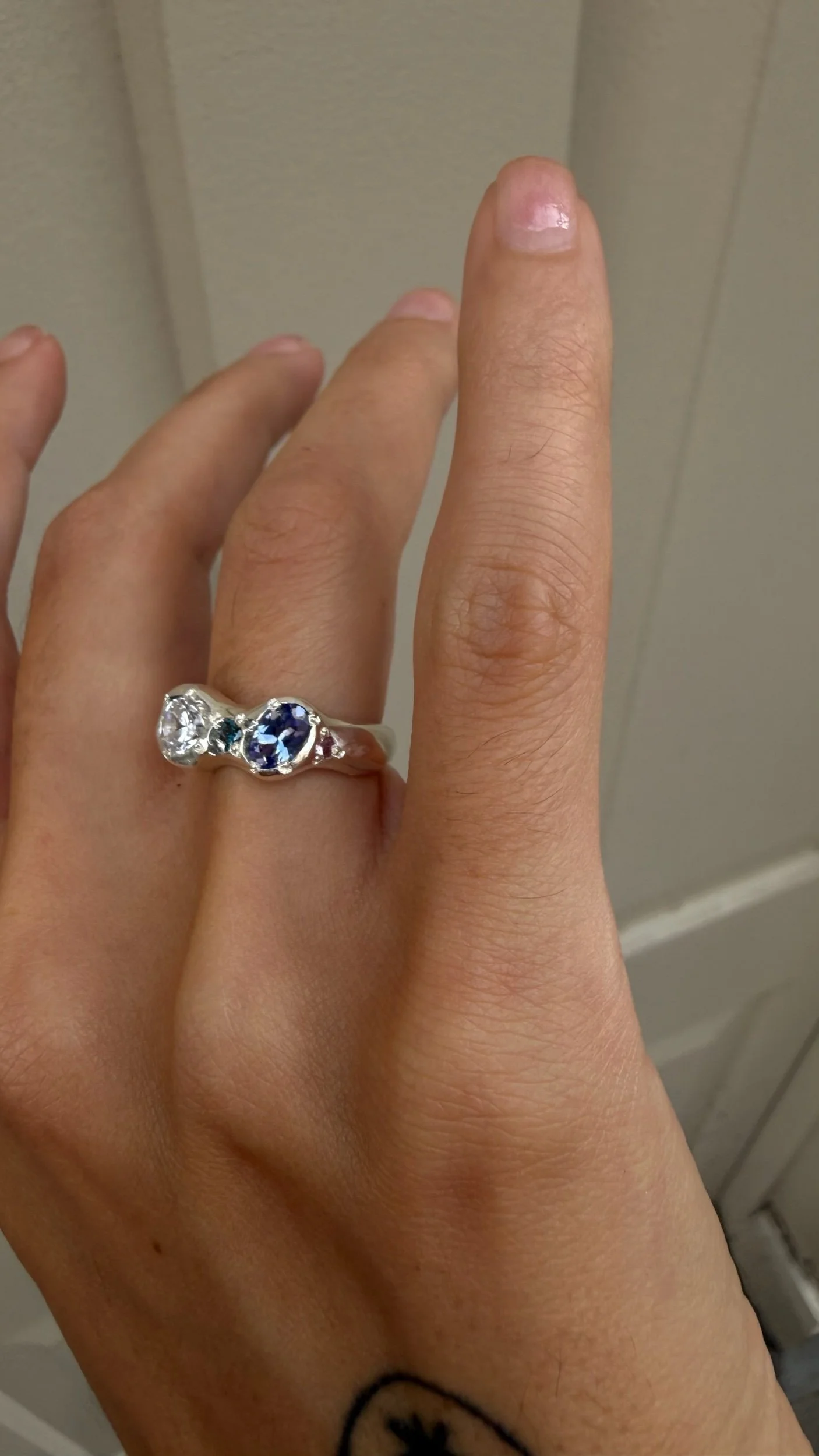A silver ring with a white and purple stone as the focus on a hand