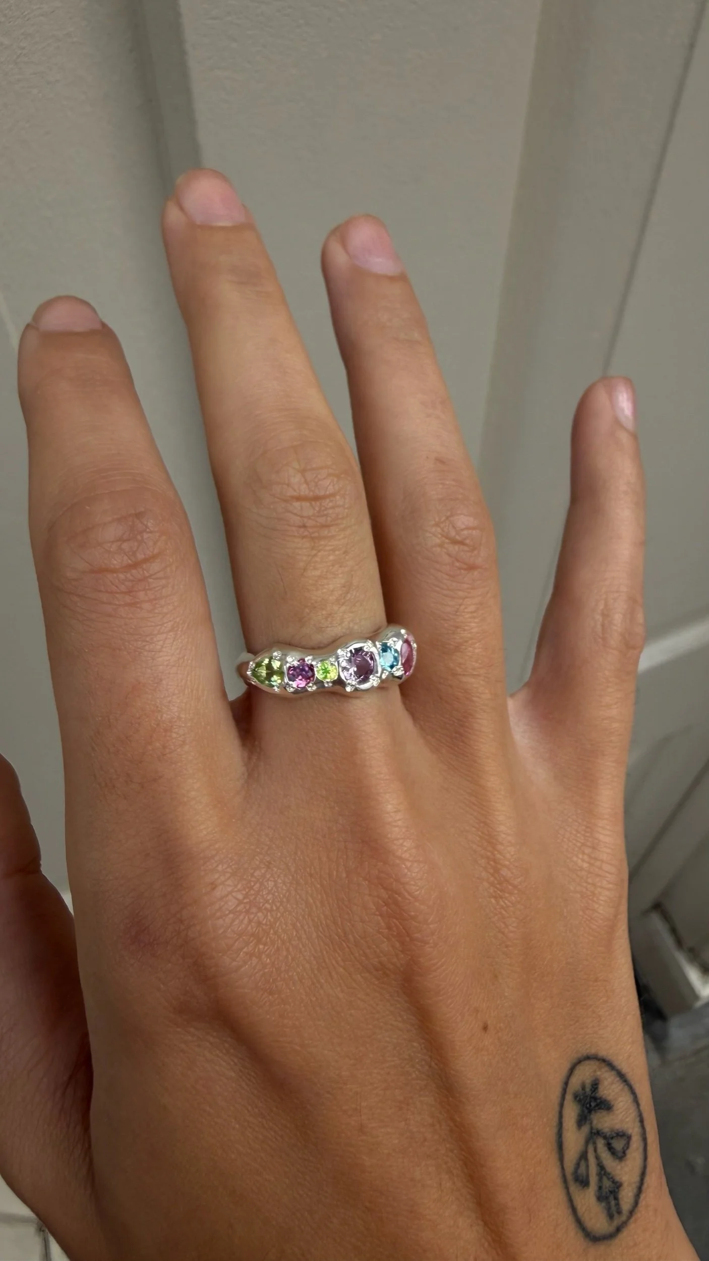 A molten silver ring with multicoloured gemstones photographed on a hand