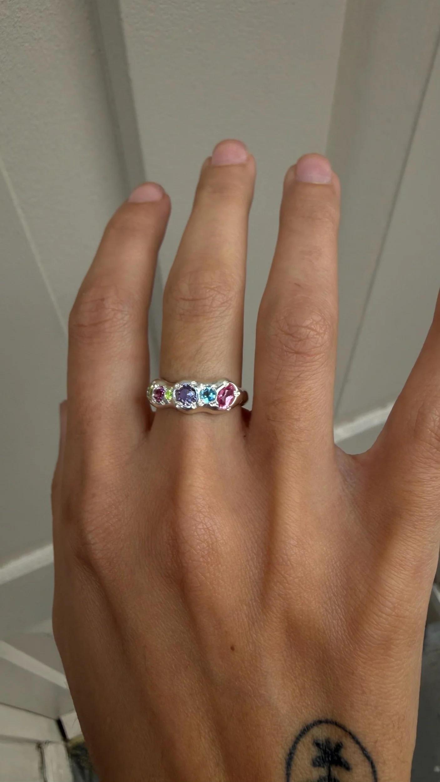 A molten silver ring with multicoloured gemstones photographed on a hand