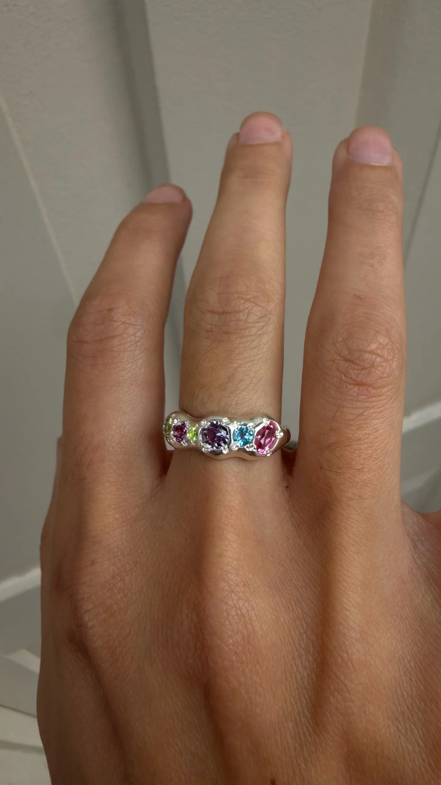 A molten silver ring with multicoloured gemstones photographed on a hand