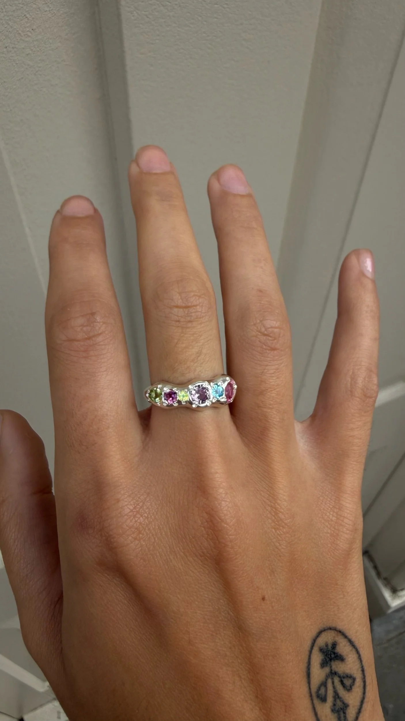 A molten silver ring with multicoloured gemstones photographed on a hand