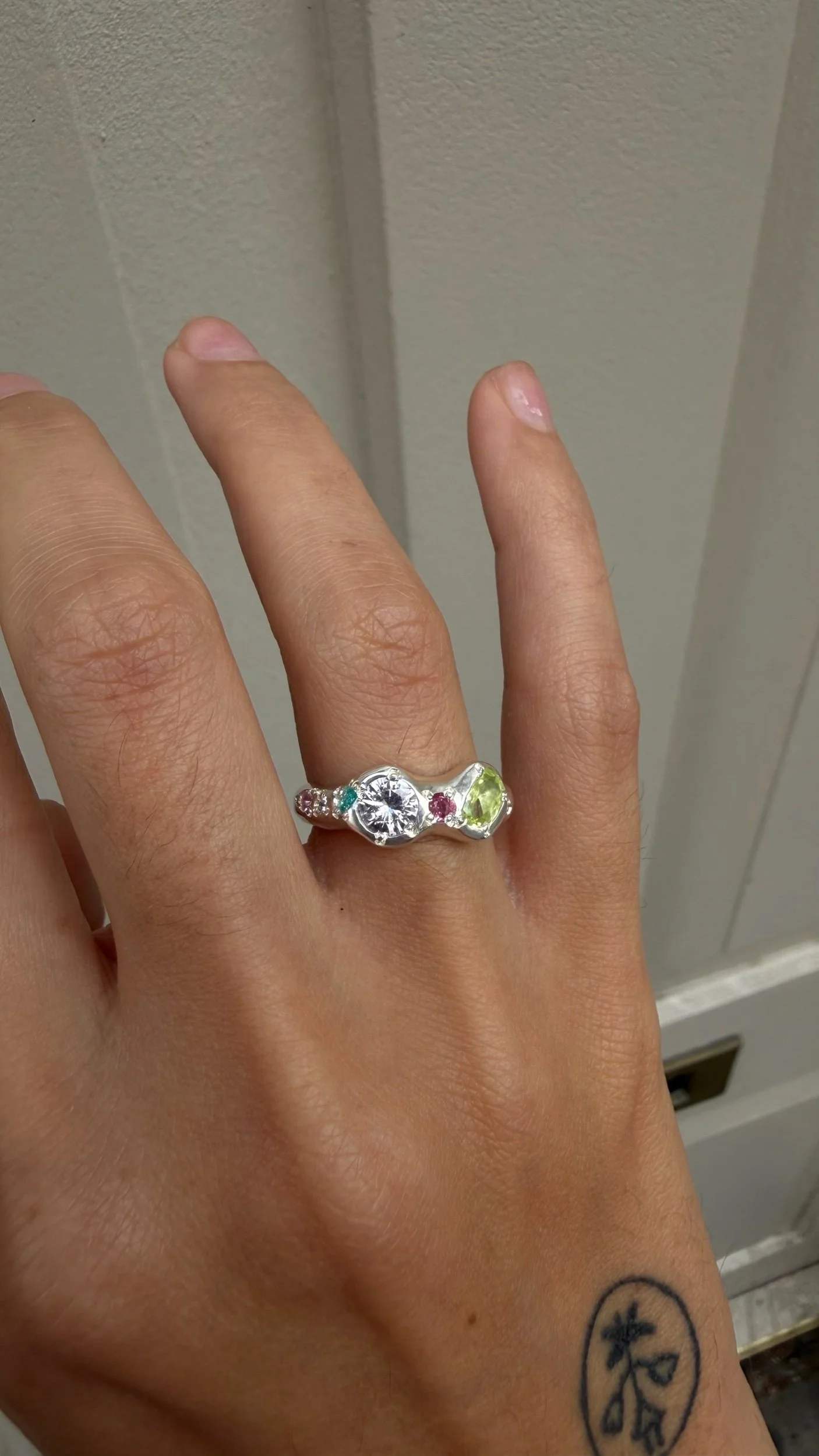 A silver ring with a pastel pink sand green stone as the focus on a hand
