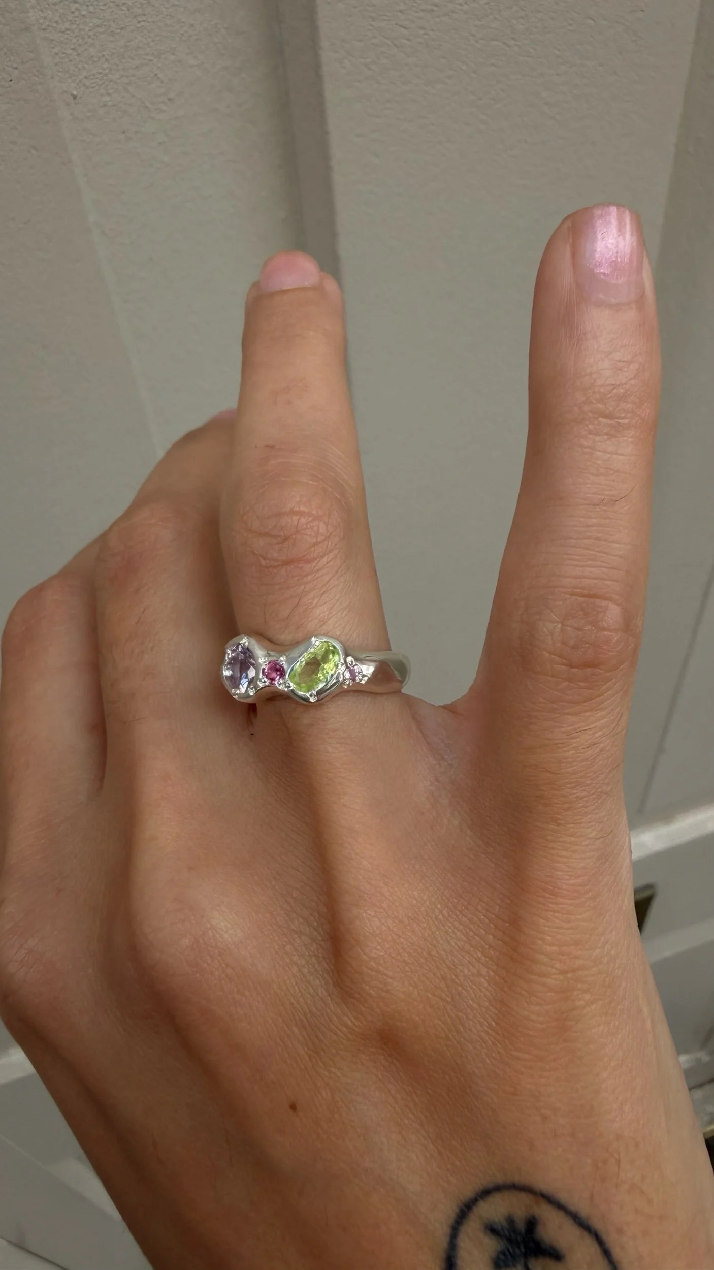 A silver ring with a pastel pink and green stone as the focus on a hand