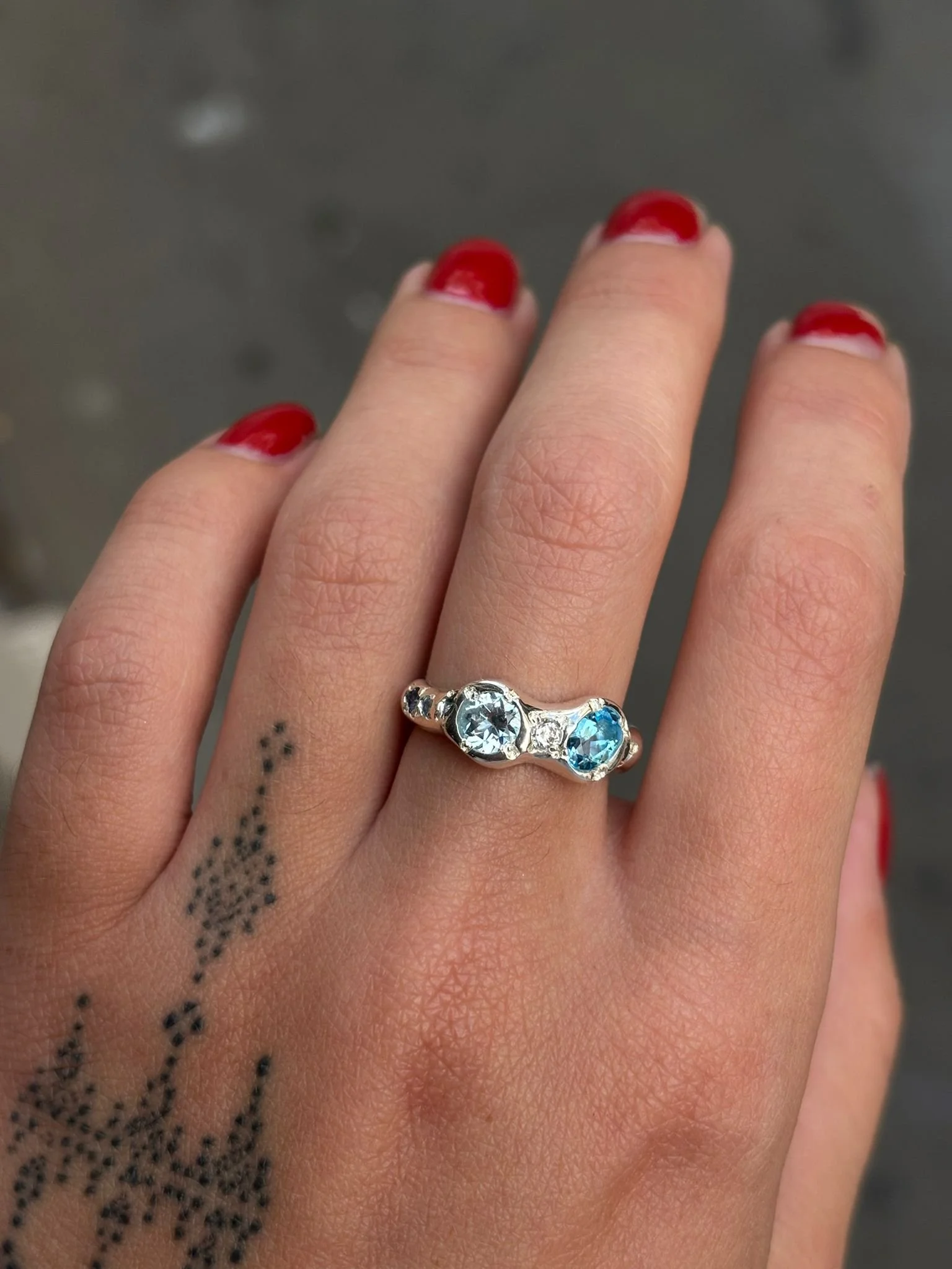A molten silver ring with blue gemstones photographed on a hand