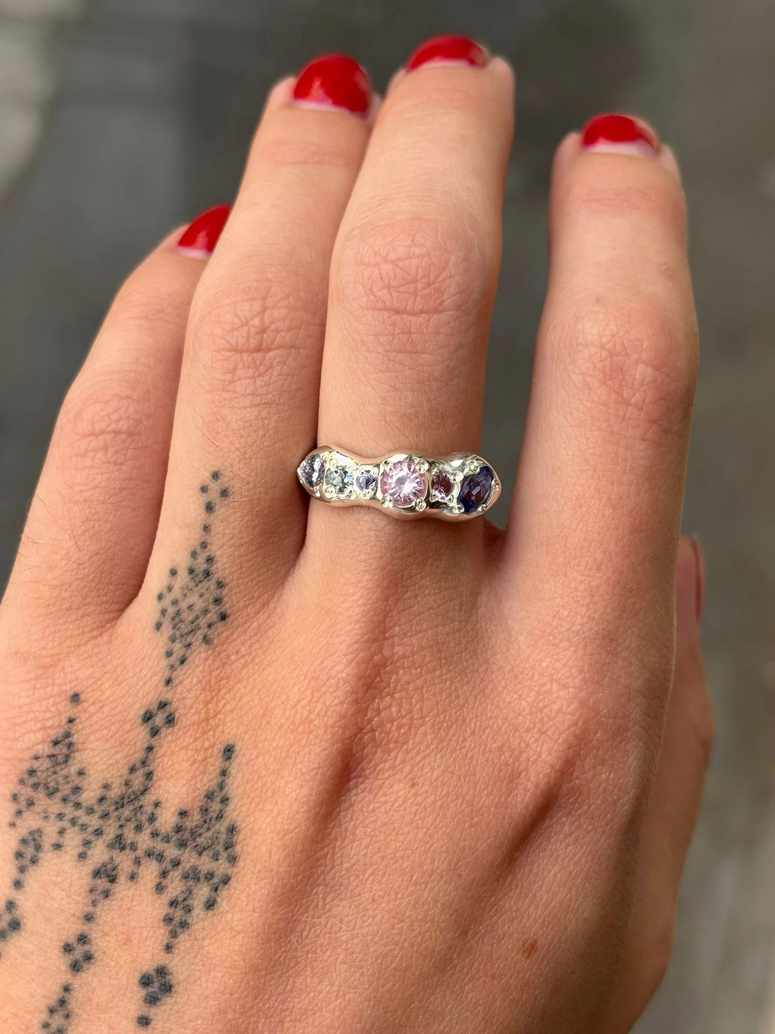 A molten silver ring with purple and pink gemstones photographed on a hand