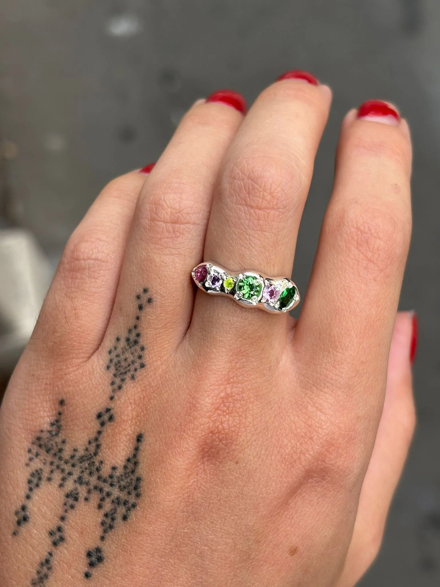 A molten silver ring with multicoloured gemstones photographed on a hand
