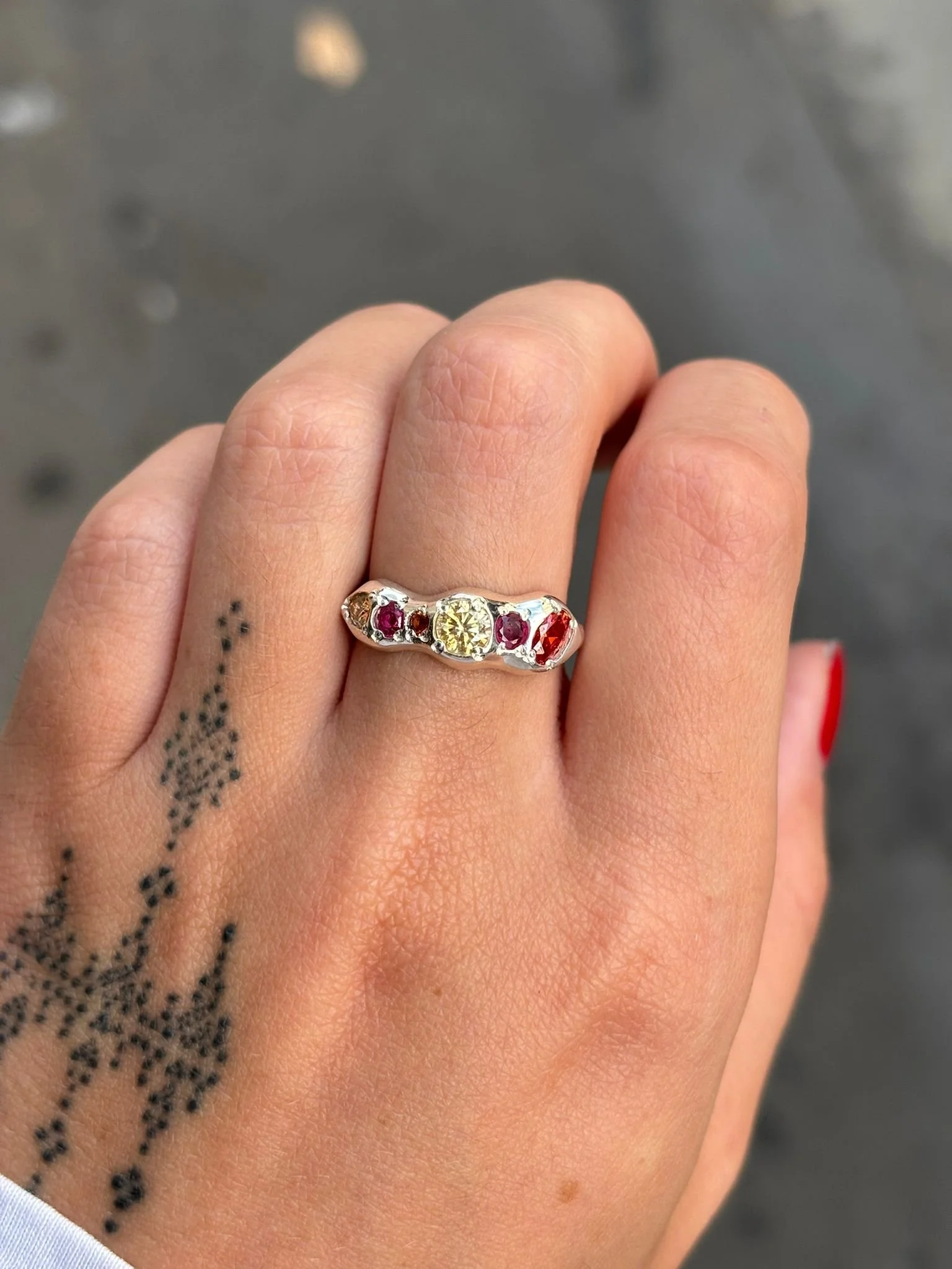 A molten silver ring with orange gemstones photographed on a hand