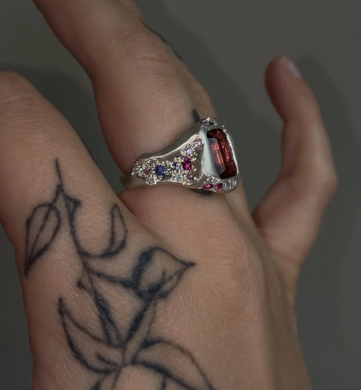 A sterling silver signet ring with a central large pink tourmaline and smaller stones down the sides in pink and purple on a hand