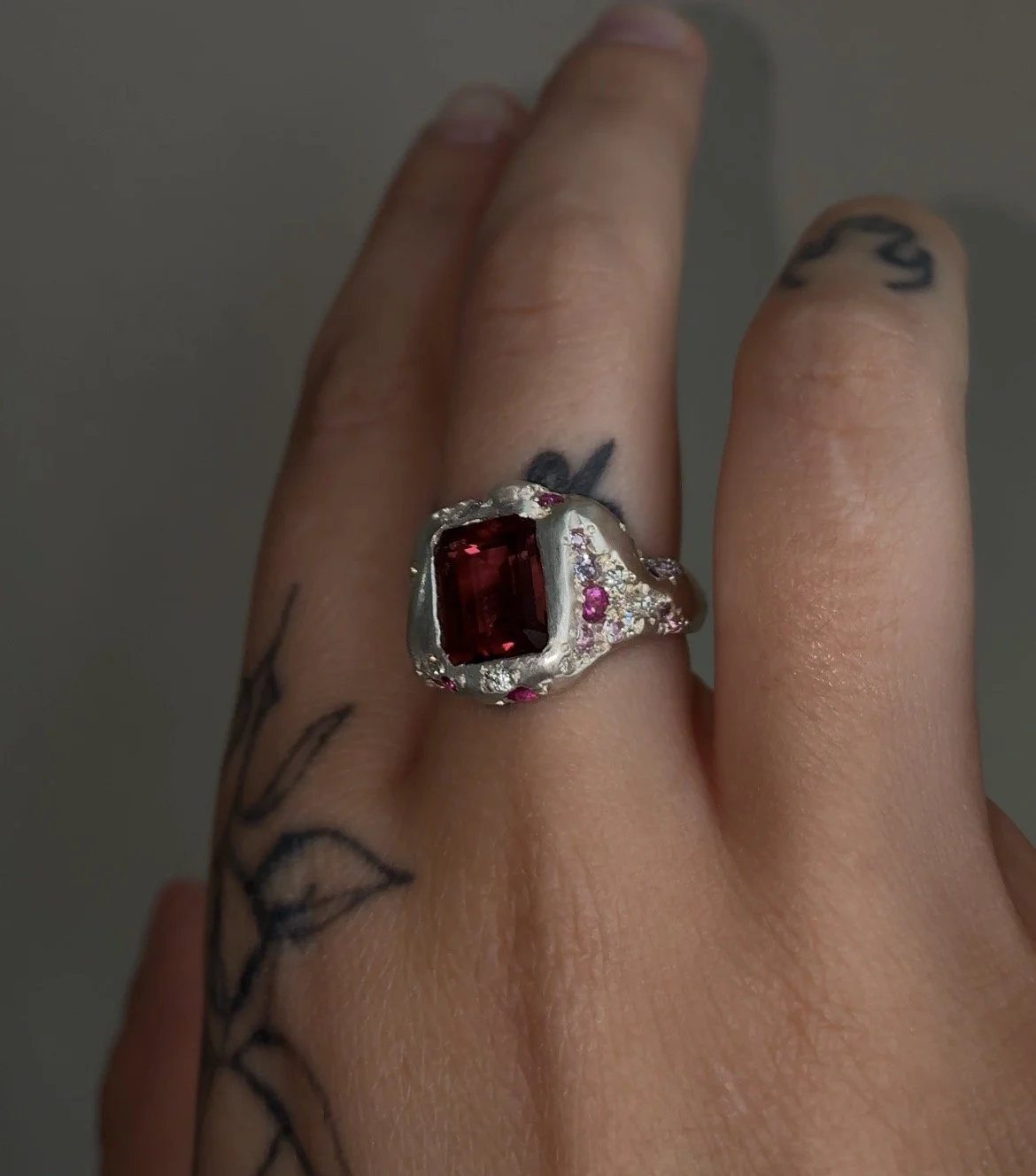 A sterling silver signet ring with a central large pink tourmaline and smaller stones down the sides in pink and purple on a hand