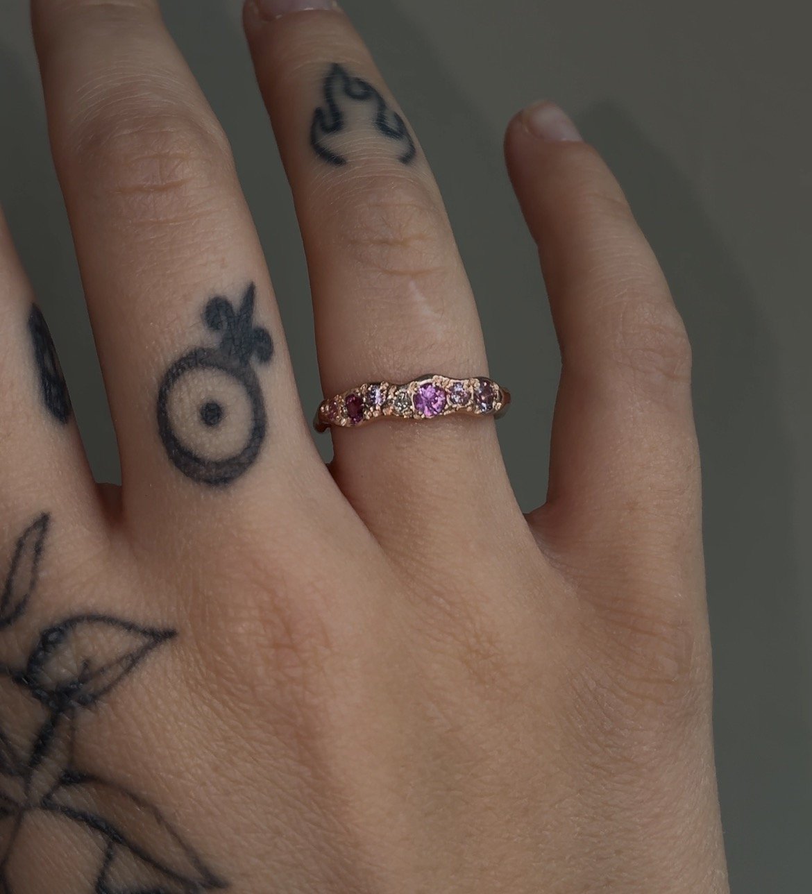 A molten red gold ring with pink gemstones photographed on a hand