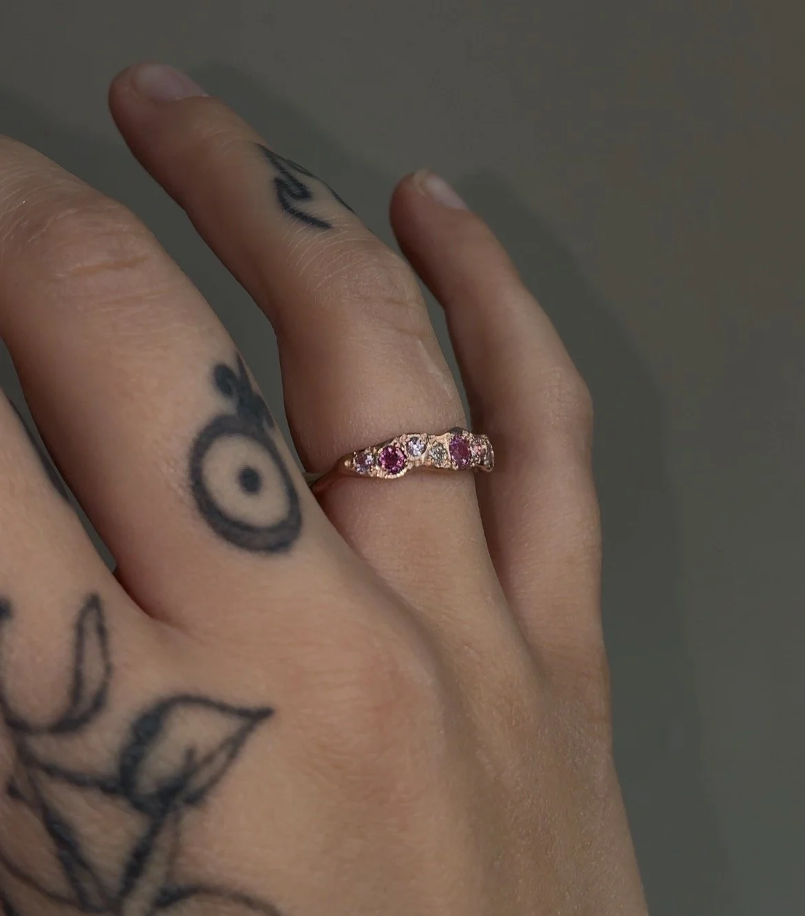 A molten red gold ring with pink gemstones photographed on a hand