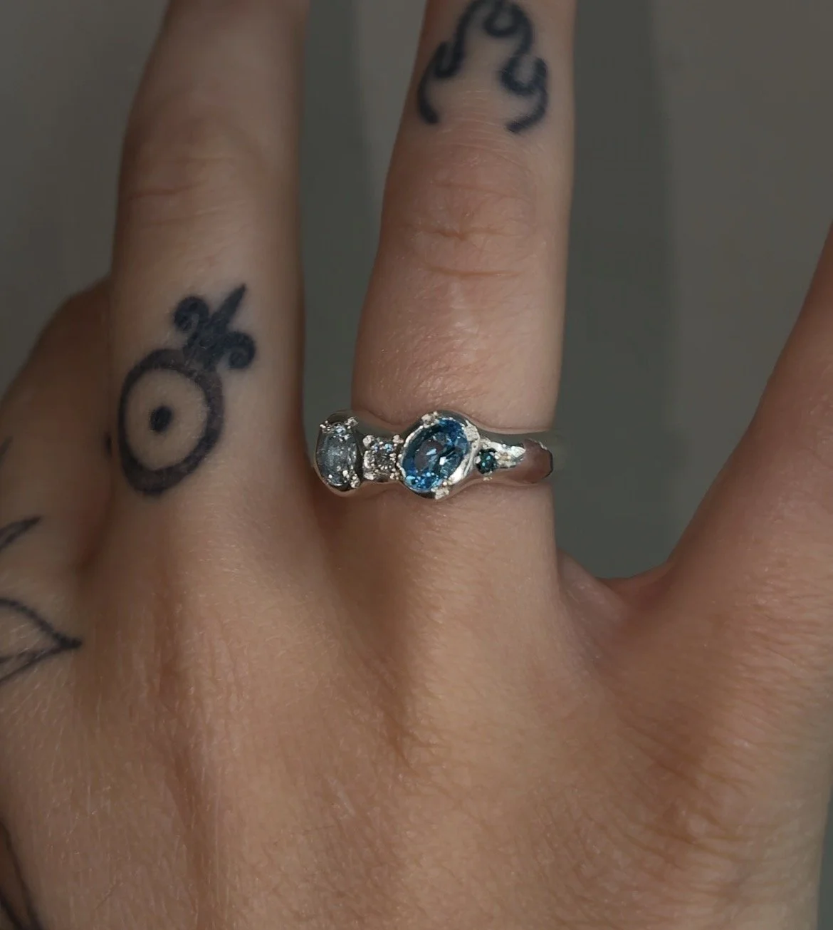 A molten silver ring with blue gemstones photographed on a hand
