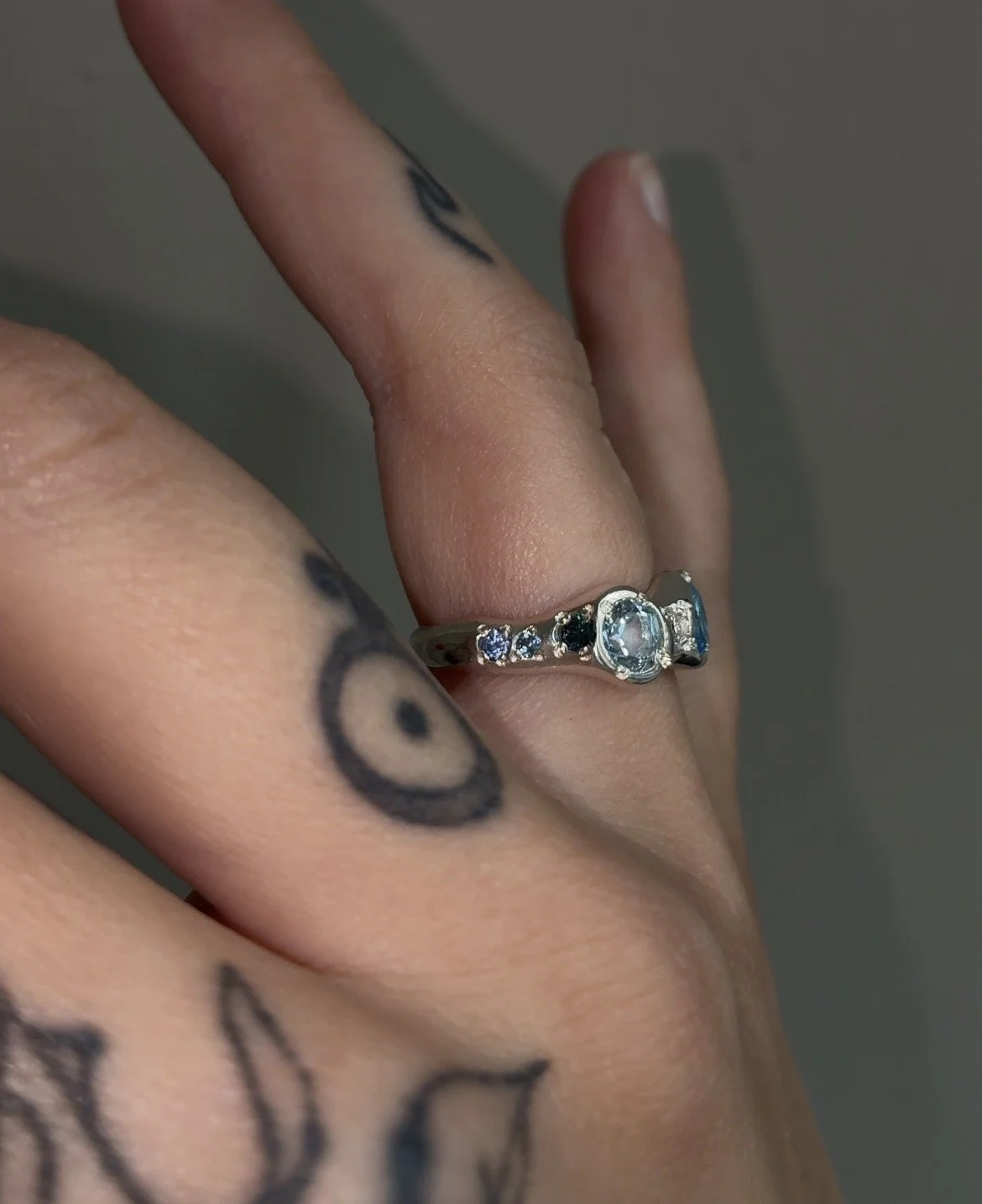 A molten silver ring with blue gemstones photographed on a hand