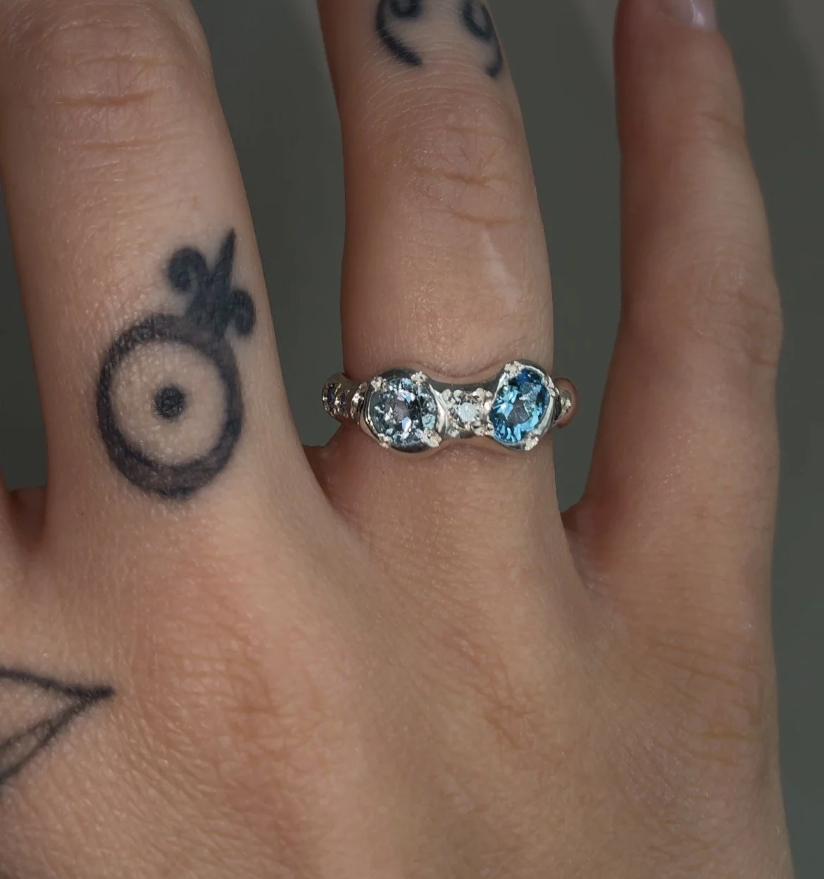 A molten silver ring with blue gemstones photographed on a hand