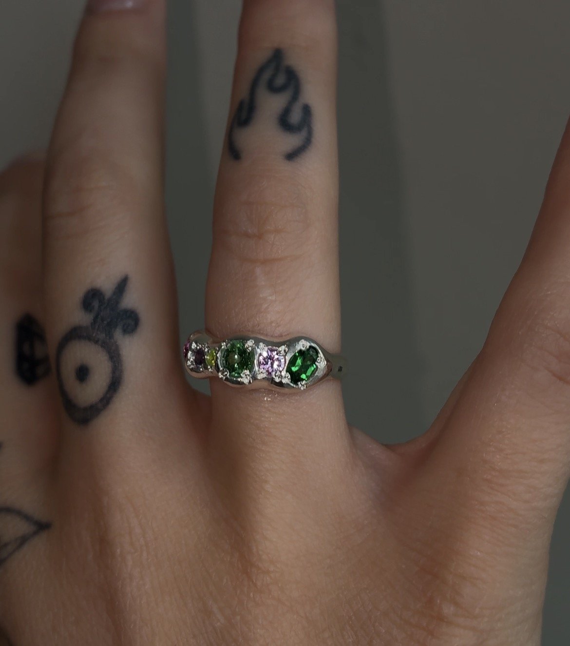 A molten silver ring with multicoloured gemstones photographed on a hand