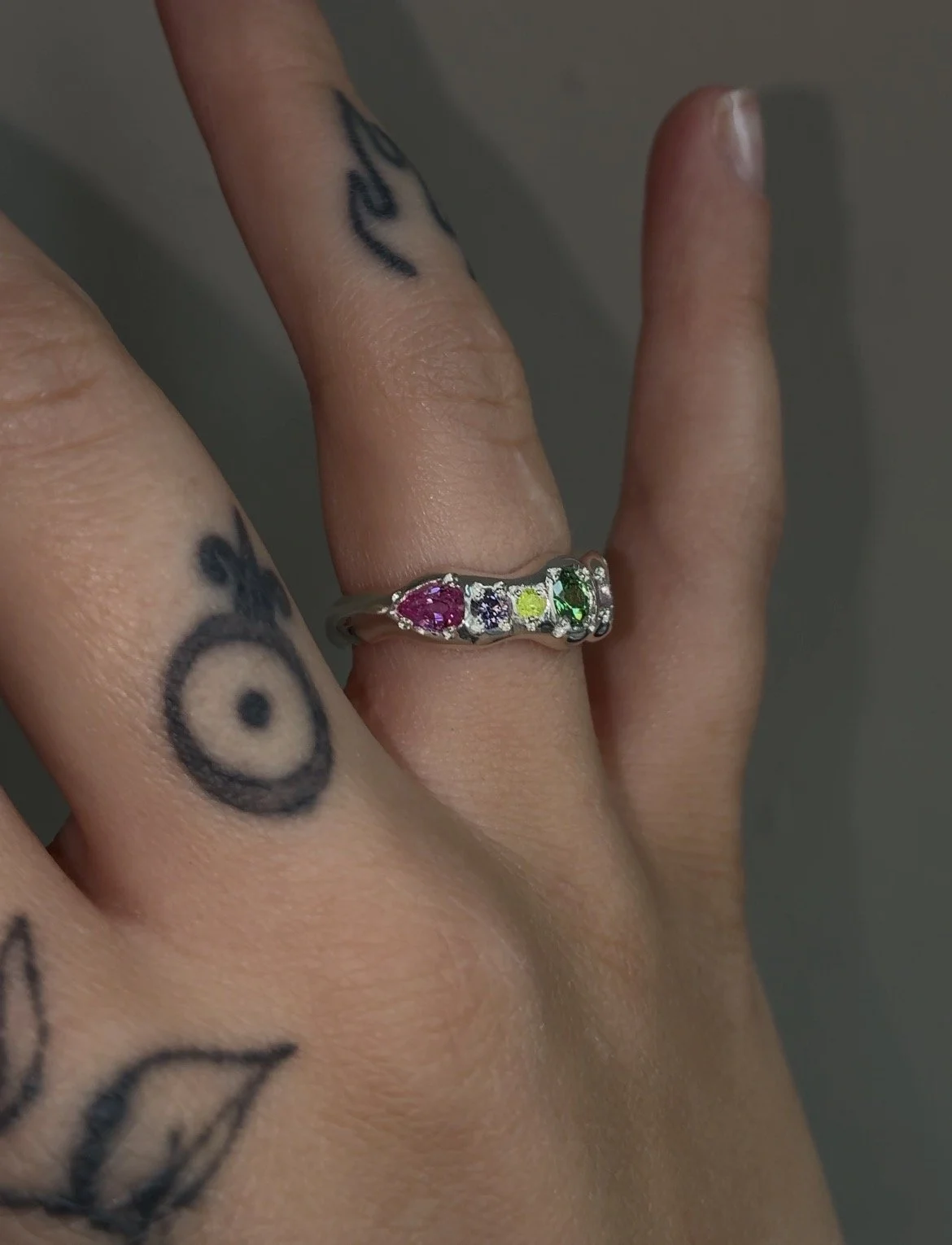 A molten silver ring with multicoloured gemstones photographed on a hand