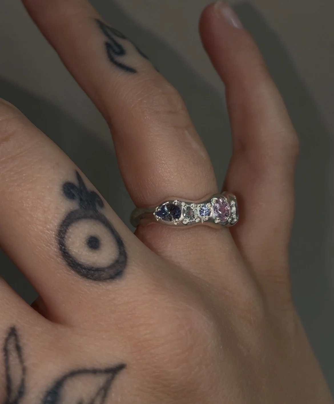 A molten silver ring with purple and pink gemstones photographed on a hand