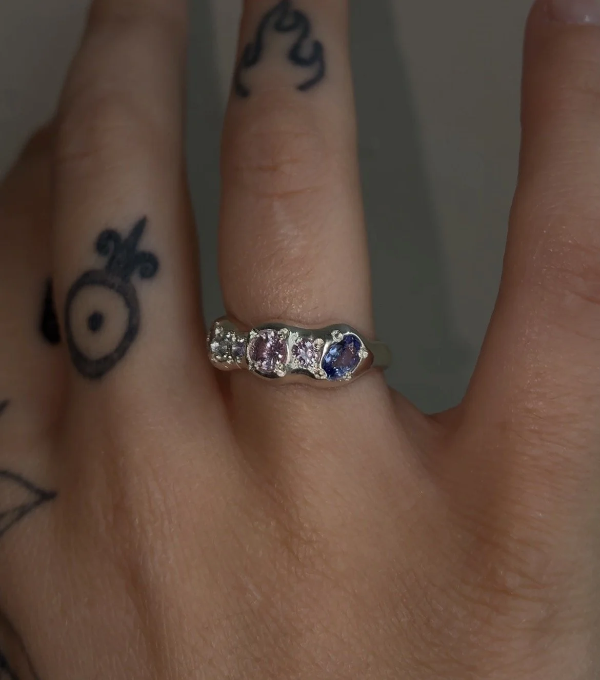 A molten silver ring with purple and pink gemstones photographed on a hand