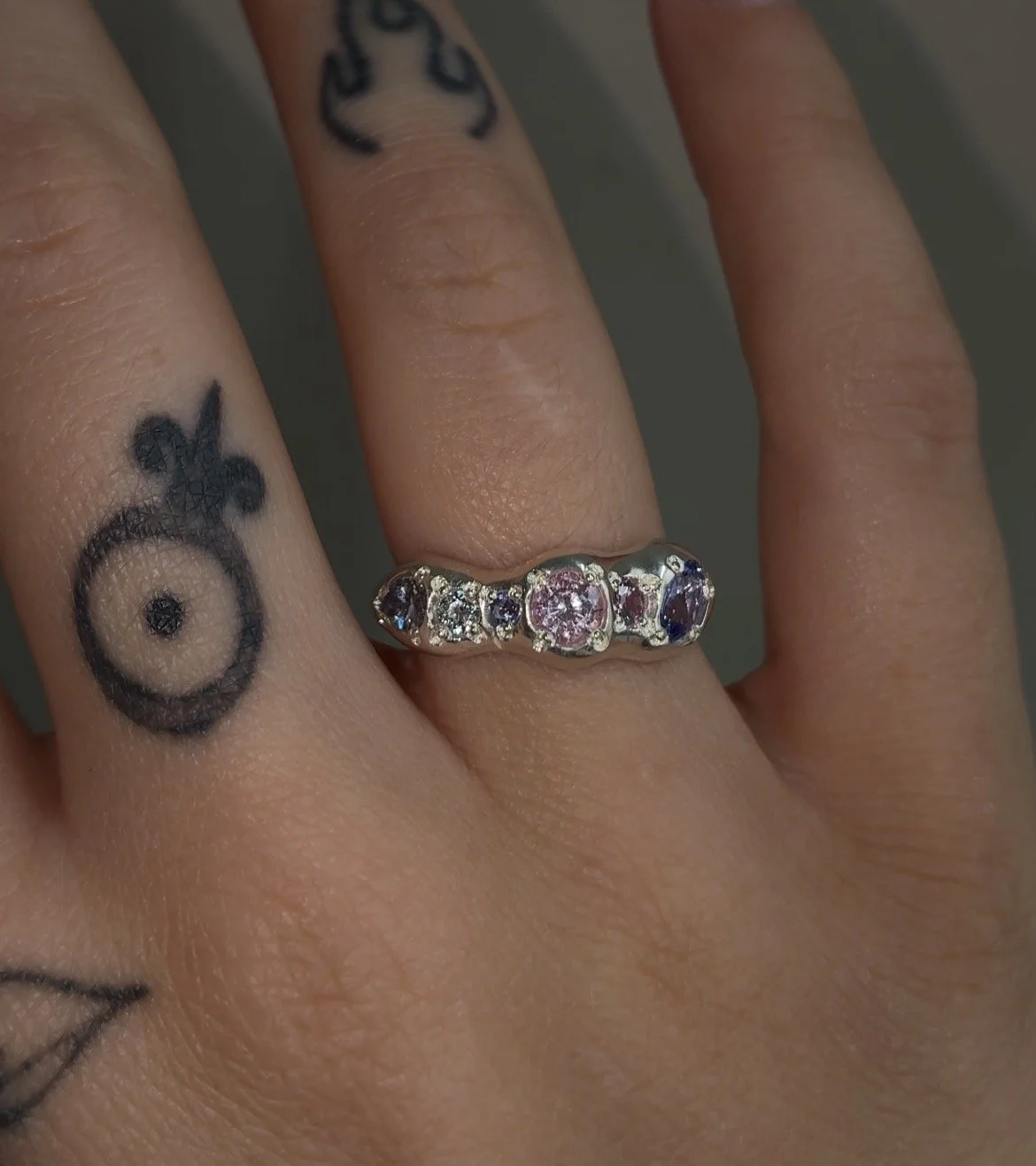 A molten silver ring with purple and pink gemstones photographed on a hand