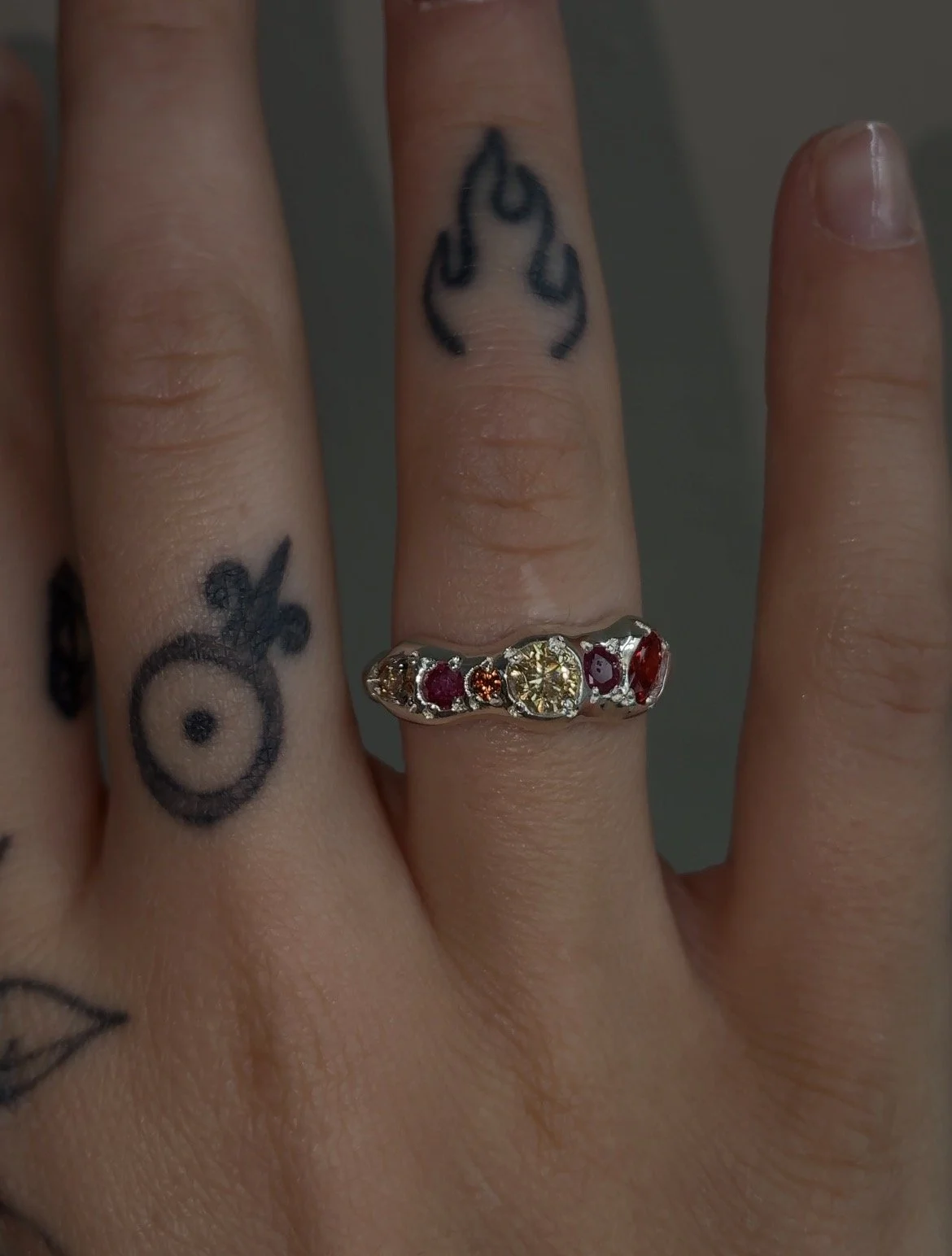 A molten silver ring with orange gemstones photographed on a hand