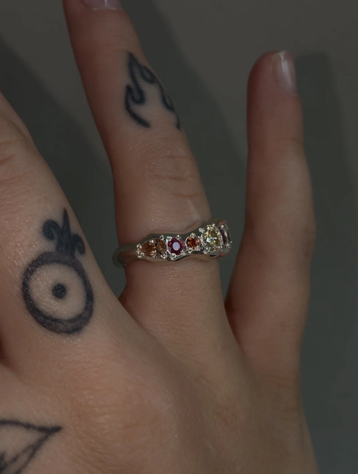 A molten silver ring with orange gemstones photographed on a hand