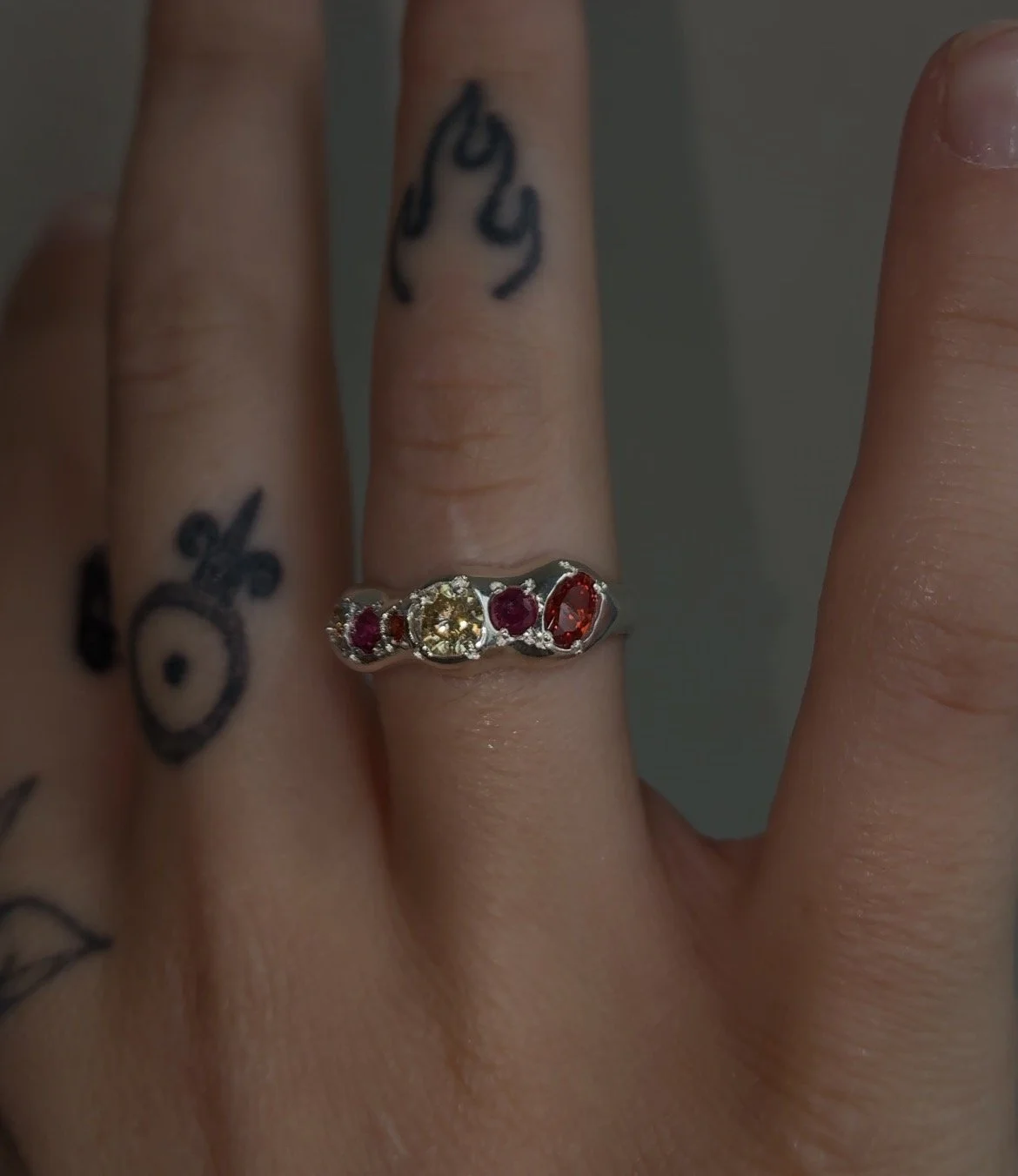 A molten silver ring with orange gemstones photographed on a hand