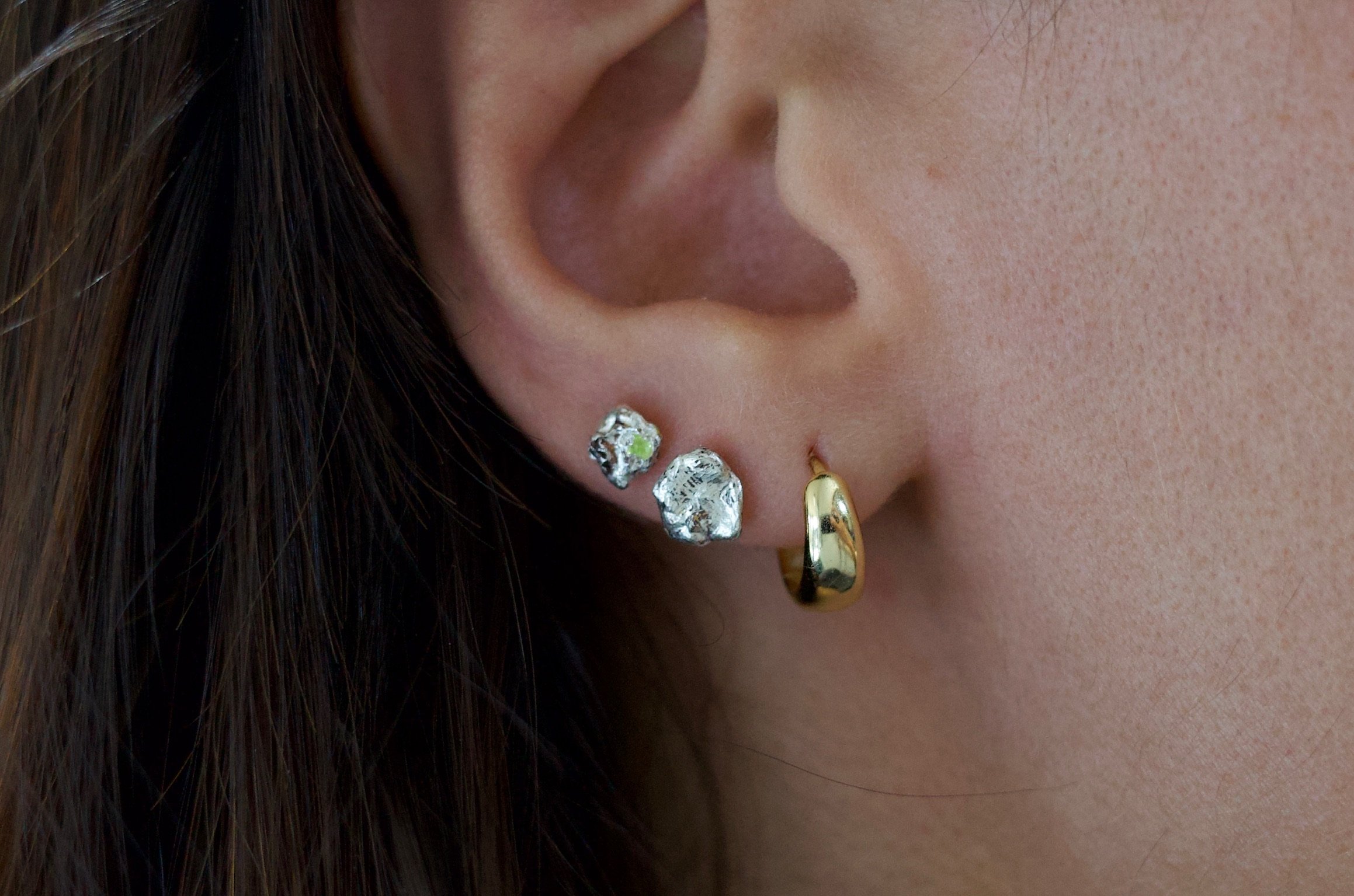 Textured sterling silver studs with a neon green stone in one stud. The studs are mismatched and in an ear