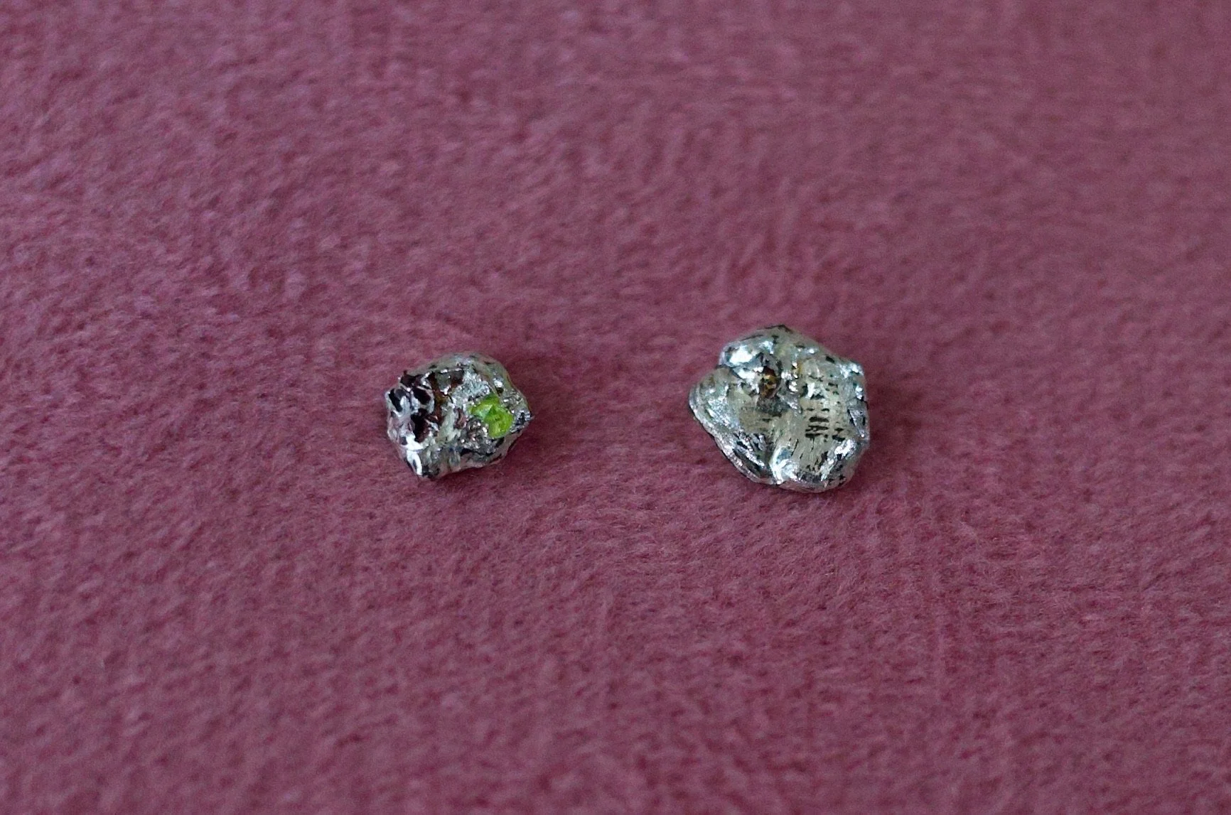 Textured sterling silver studs with a neon green stone in one stud. The studs are mismatched
