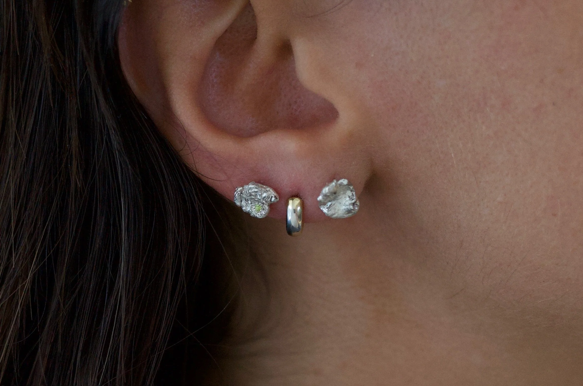 Textured sterling silver studs with a neon green stone in one stud. The studs are mismatched and in an ear