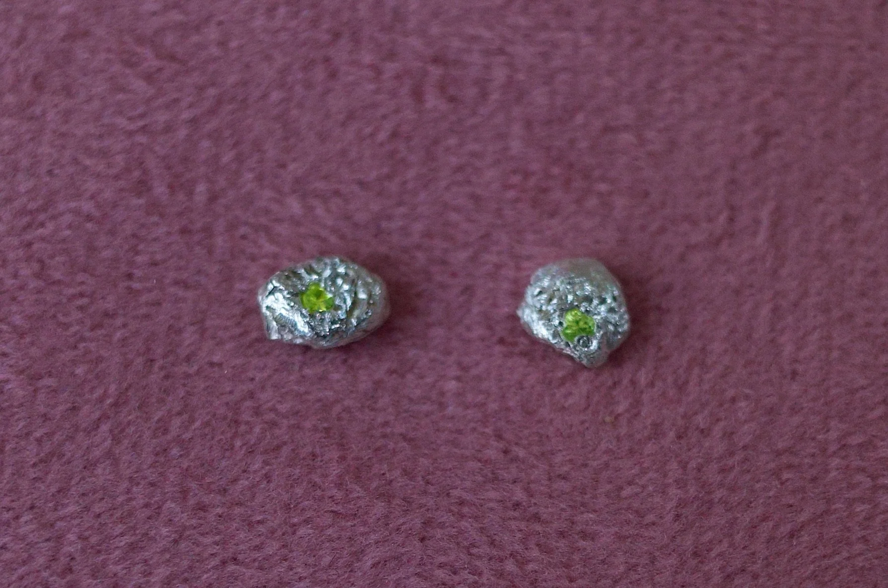 Textured sterling silver studs with a neon green stone in each stud. The studs are mismatched