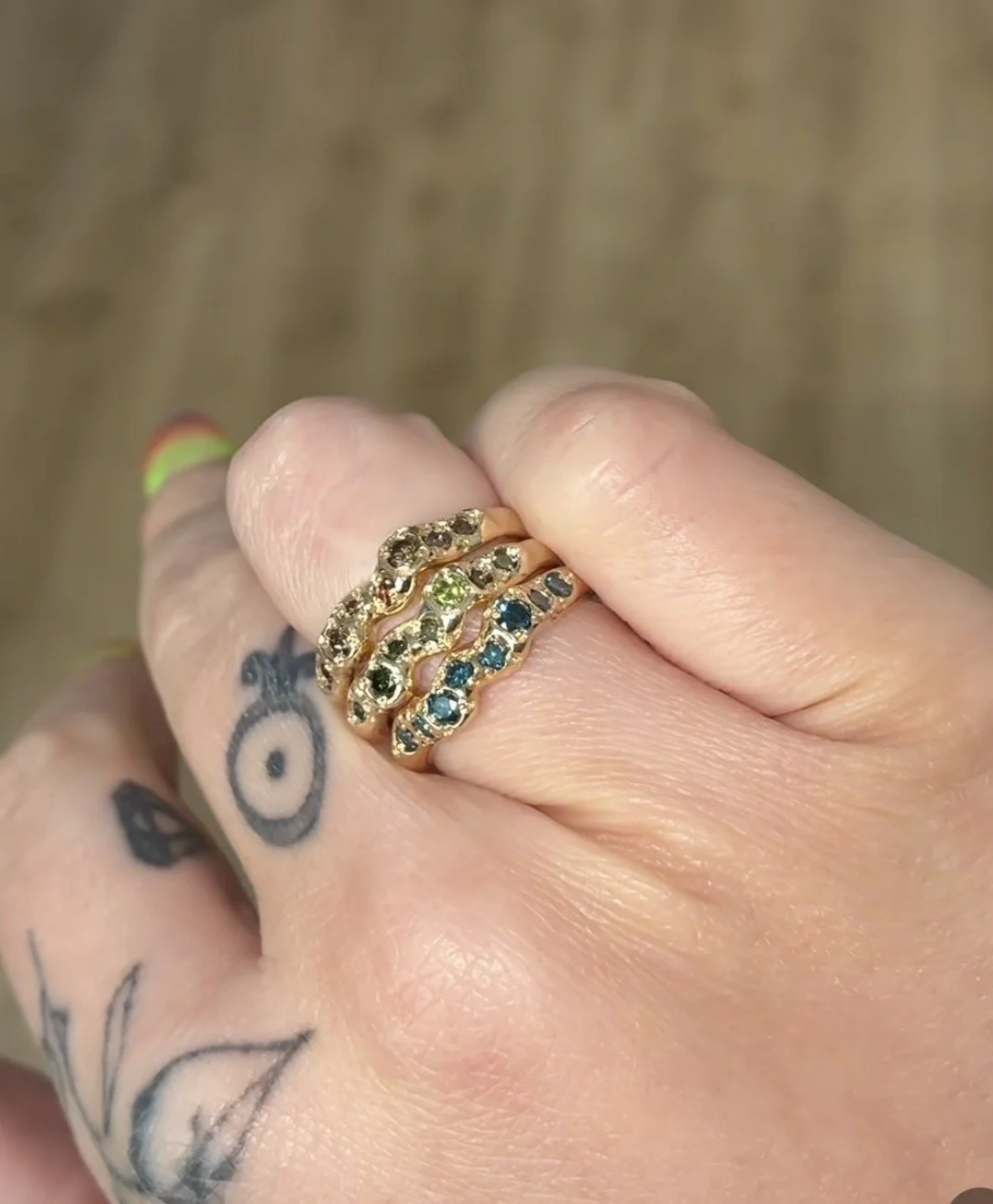 A stack of molten bands with different colour diamonds in them on a woman's hand