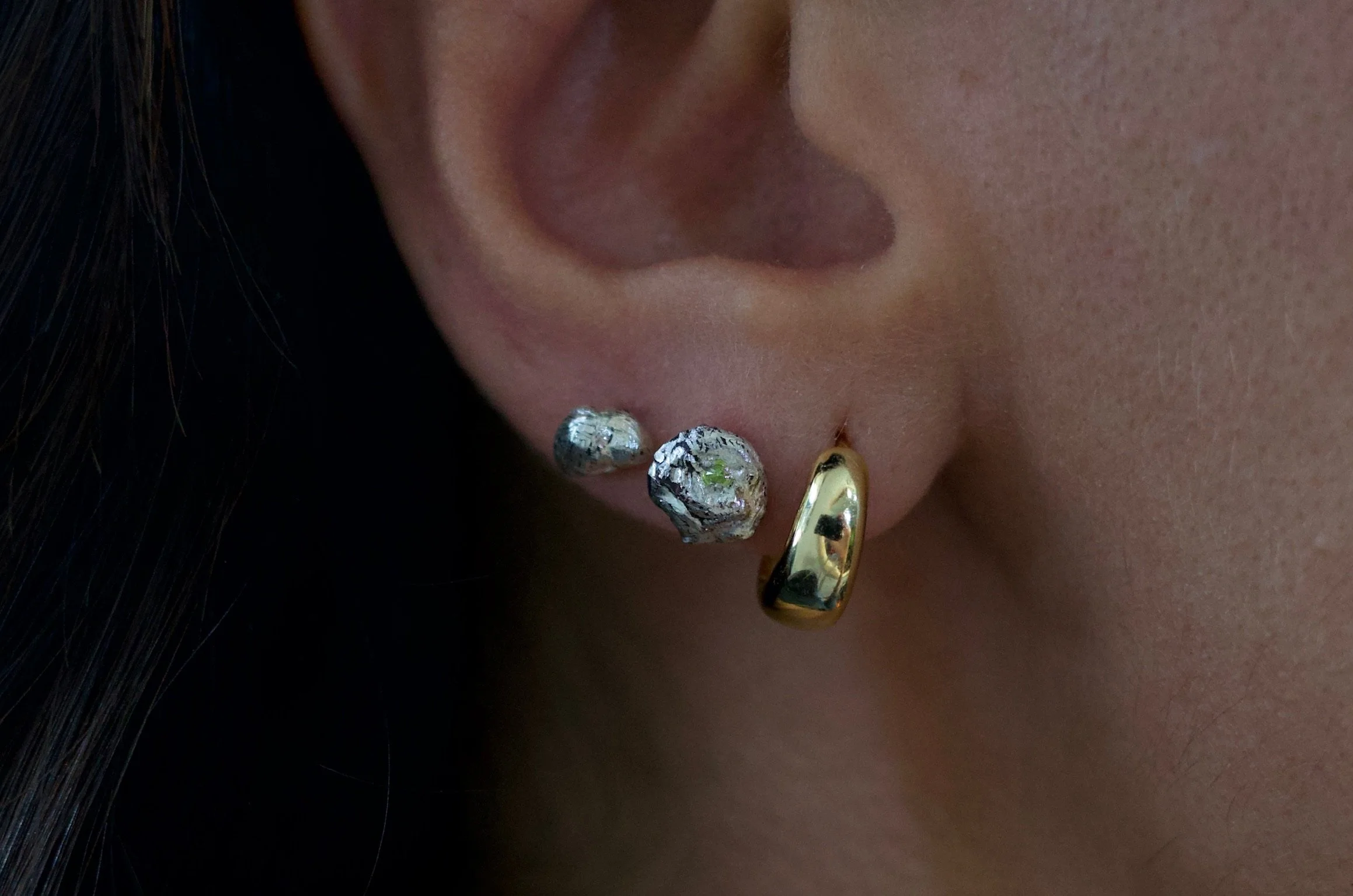 Textured sterling silver studs with a neon green stone in one stud. The studs are mismatched and in an ear